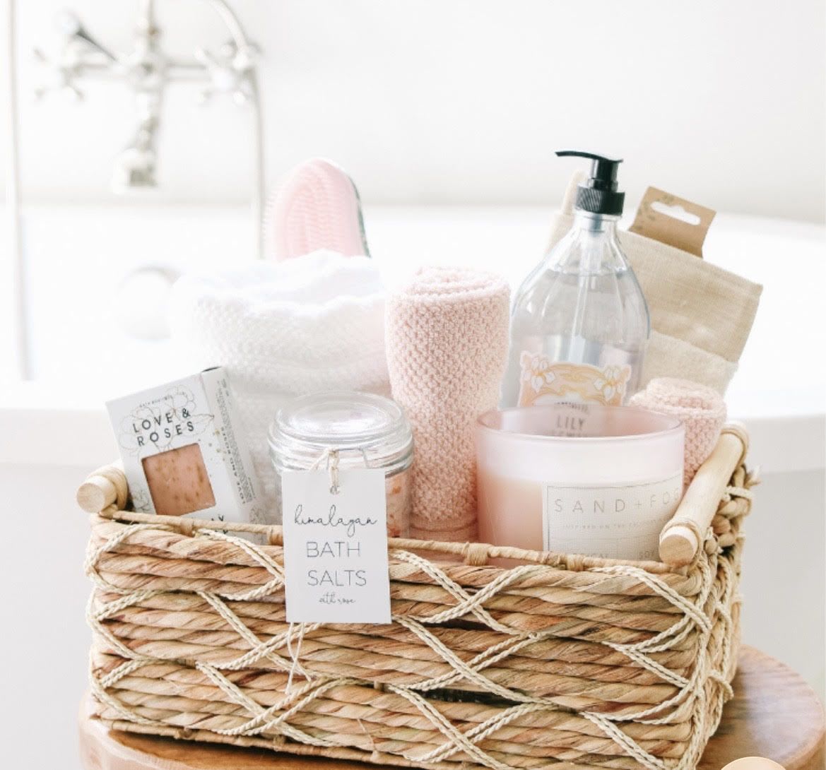 Pamper Bath Set - Soft blush and creamy white spa essentials arranged in a woven basket create a calm, pampering gift perfect for Mother's Day, birthdays, anniversaries, or simply to say "thinking of you." This pamper bath set presents bath salts, a glass candle, boxed soap, a pump bottle, and crocheted washcloths in a tidy, feminine palette that reads as thoughtful self-care - ideal for Valentine's Day, Graduation, or to celebrate a special woman in your life.  The basket includes a jar of bath salts, a scented glass candle, a boxed soap, a pump bottle (lotion or wash), neatly rolled washcloths, and a crocheted cloth, all tucked into natural straw with a paper gift bag for easy presenting. Soft pinks, whites, and neutral tones make the set feel soothing and elevated without being fussy.  Give this as a holiday hostess gift, an anniversary surprise, or a simple "congrats" or Admin Professionals' Week thank-you that helps someone unwind. Sizes and exact scents vary by stock; items are arranged for a ready-to-gift presentation and include everything needed for an at-home spa moment. 