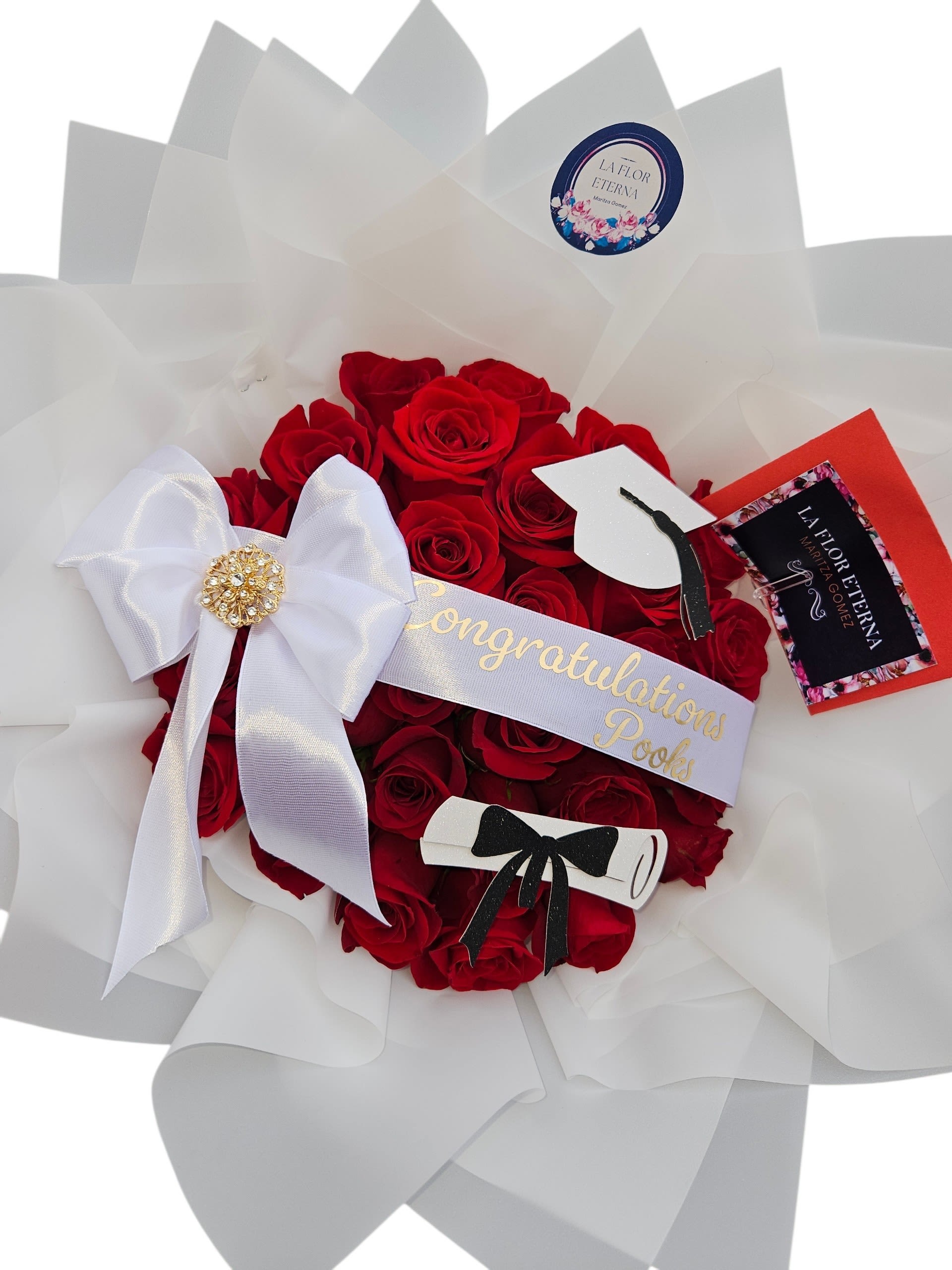 Congratulation roses Bouquet  - A concentrated cloud of velvety red roses creates a bold, romantic statement-designed as a congratulatory bouquet for graduations and big achievements. The tight, rounded cluster of blooms reads formal and celebratory, sending a clear message of pride and admiration to the person you're honoring.  Each arrangement features red roses wrapped in layered black or white paper for striking contrast, finished with a wide white satin ribbon, large decorative bow, and a jeweled or gold-toned brooch accent. Graduation-themed details-a printed "Congratulations" sash and a small graduation cap topper-turn this floral gift into a keepsake presentation with a polished, luxury feel.  Perfect for the new graduate, award recipient, or anyone marking a milestone, this bouquet looks impressive straight out of the box and is ready to present at ceremonies or celebratory gatherings. Sized as a compact, hand-held arrangement, it arrives gift-ready with our brand sticker and decorative round label-no extra wrapping needed.