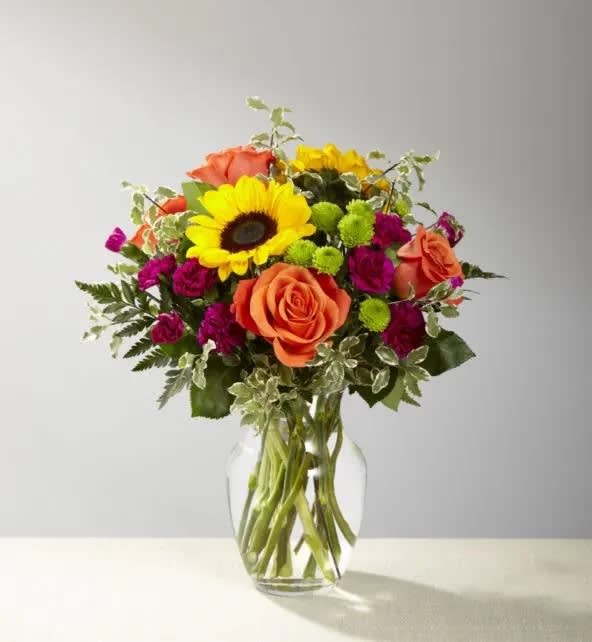 Color Craze   - **Due to current flower shortages, substitutions are likely, though we will always try to keep designs as close to the original as possible**  Color Craze Bouquet blooms with a vibrant energy to create a special moment for your recipient! Our floral professionals weave together a blend of orange roses, sunflowers, violet mini carnations, green button poms, and lush greens to create an incredible gift. Presented in a clear glass vase, this truly colorful display of fresh flowers is ready to send your warmest birthday, thank you, or get well wishes straight to their door. Regular bouquet is approx. 15"H x 12"W  Care Instructions for Fresh Flowers: Check water level upon arrival, and add very cold water if needed. Keep any arranging foam saturated, and vases very full of water. Keep cut flowers out of direct sunlight and avoid excessively hot or cold areas. Place a tray under flowers and plants to protect decorative surfaces.   Available for delivery to East Moline, Moline, Rock Island, Silvis, Colona, Hampton, Coal Valley, Milan, Davenport, and Bettendorf. 