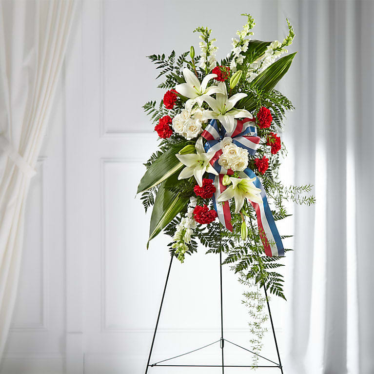Stars of Life Standing Spray - STARS OF LIFE STANDING SPRAY Share your respects with flowers that evoke the true spirit of a hero. Our Stars of Life spray is accented with a patriotic ribbon and features a gorgeous yet timeless collection of carnations, snapdragons, lilies and roses.  Please Note: The bouquet pictured reflects our original design for this product. While we always try to follow the color palette, we may replace stems to deliver the freshest bouquet possible.  DETAILS The Standard Spray is approximately 38"H  Arrives attached to an eaels ready to display.  BLOOM DETAILS Carnation Lily Rose Snapdragon