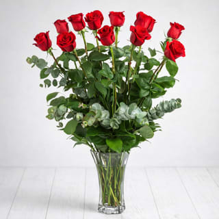 Dozen Red Roses in a Glass Vase - Product Description  This classic dozen red roses Valentine’s Day flower arrangement in a clear glass vase is hand designed by a local East Moline florist with delivery available.  Our Dozen Red Roses in a Glass Vase features premium red roses arranged with fresh greenery for a timeless, romantic look that speaks straight from the heart, with minor variations reflecting seasonal availability.  Dozen Red Roses in a Glass Vase is available for Valentine’s Day flower delivery in East Moline, Moline, Rock Island, Silvis, Davenport, and Bettendorf, serving the Quad Cities and surrounding areas with care. These dozen red roses are the classic romantic gift! Perfect for Valentine's Day or an Anniversary.  Standard: 12 Roses Deluxe: 18 Roses  Premium: 24 Roses   APPROXIMATE DIMENSIONS: 25" H X 18" W