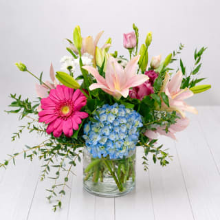 Mixed bouquet with pink lilies, blue hydrangea, and a pink gerbera daisy in a glass vase