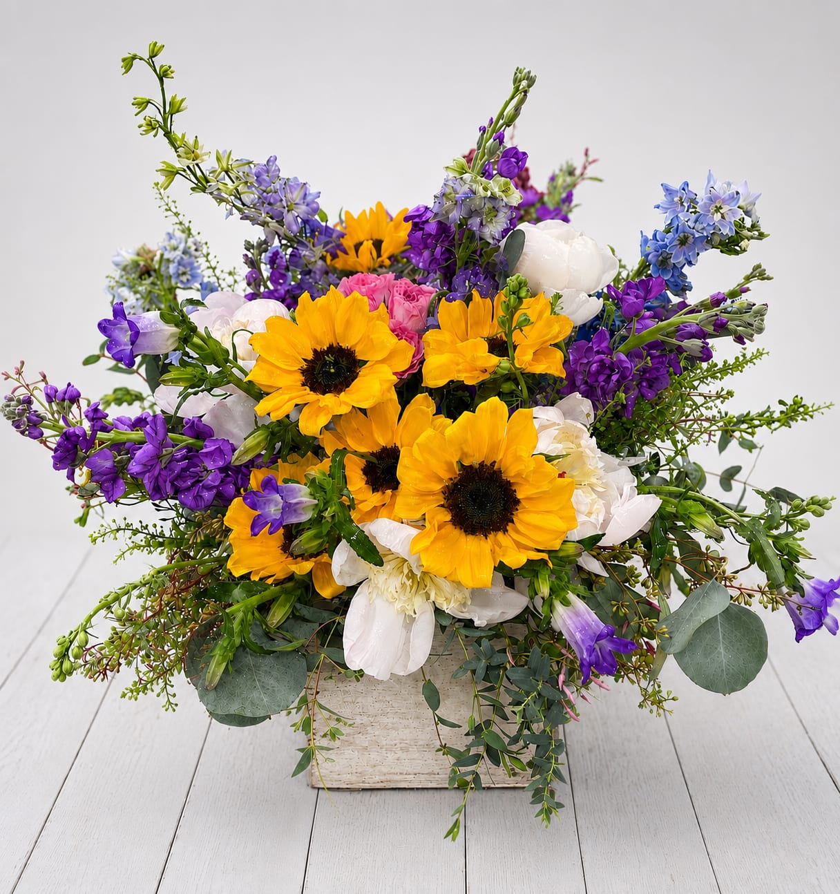 Bright mixed bouquet with yellow sunflowers, purple blooms, and white flowers in a square container