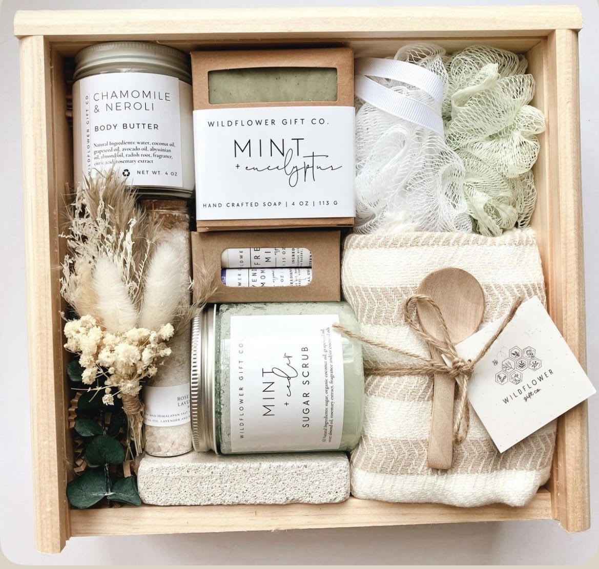 Mint &amp; Wildflower bath set - Soft, spa-inspired tones set the scene: the Mint &amp; Wildflower bath set is a calming gift-box arrangement perfect for a thank-you, birthday, or anytime self-care treat. Designed as a gift-ready presentation, this bath set reads like a mindful pause for the person you're thinking of-she'll feel cared for by the gentle mix of cream, beige, muted greens and the small bundle of dried botanicals that give it a handcrafted, natural touch.  Inside a wooden gift box you'll find labeled jars and boxes including chamomile &amp; neroli body butter, mint &amp; eucalyptus soap, and a mint sugar scrub, plus a small jar and a rolled towel tucked beside a loofah sponge. Twine ribbon and a gift tag finish the presentation, creating a cohesive, rustic look that feels both elegant and approachable. The compact, neatly arranged items make this an easy, worry-free gift for someone who appreciates soothing scents and simple, quality bath essentials.  Ideal for sending to a friend recovering from illness, a mother needing quiet time, or a colleague deserving a thoughtful thank-you, this set arrives ready to enjoy-no wrapping required. Care is straightforward: the bath products are presented in labeled jars and boxes for easy use; keep products dry between uses and store in a cool place to preserve scent and texture.