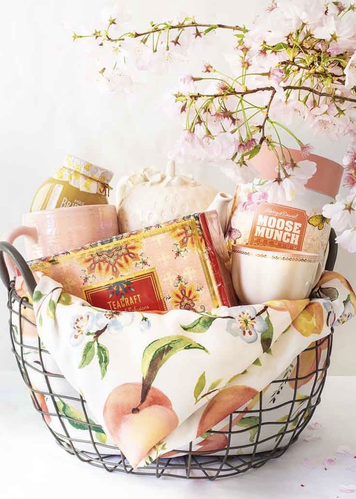 For your tea lover - Delicate cherry blossom branches arching over a charming black wire basket set the tone for this "For your tea lover" gift - a perfect tea-lover gift or spring celebration present that feels thoughtful and feminine. This floral-lined tea basket works beautifully as a birthday surprise, Mother's Day treat, or a "thinking of you" moment for someone who savors quiet, cozy rituals.   Inside the basket you'll find a soft, cheerful palette of pastel pink, cream, yellow, and orange in ceramic mugs, tea tins, and a teapot, all nestled on a floral-print fabric liner and finished in a neat gift box. The airy cherry blossom stems add seasonal height and texture, while the mix of ceramic and tin gives a pleasing contrast of smooth and metallic surfaces. Presented in a black wire basket, the arrangement stays light and elegant while keeping everything visible and ready to enjoy.  This is the kind of gift that makes the recipient feel noticed and pampered - ideal for anyone who loves afternoon tea, slow mornings, or springtime gatherings. Care is simple: the branches and boxed tea items arrive ready to display; no special upkeep required beyond arranging the blossoms to your liking.