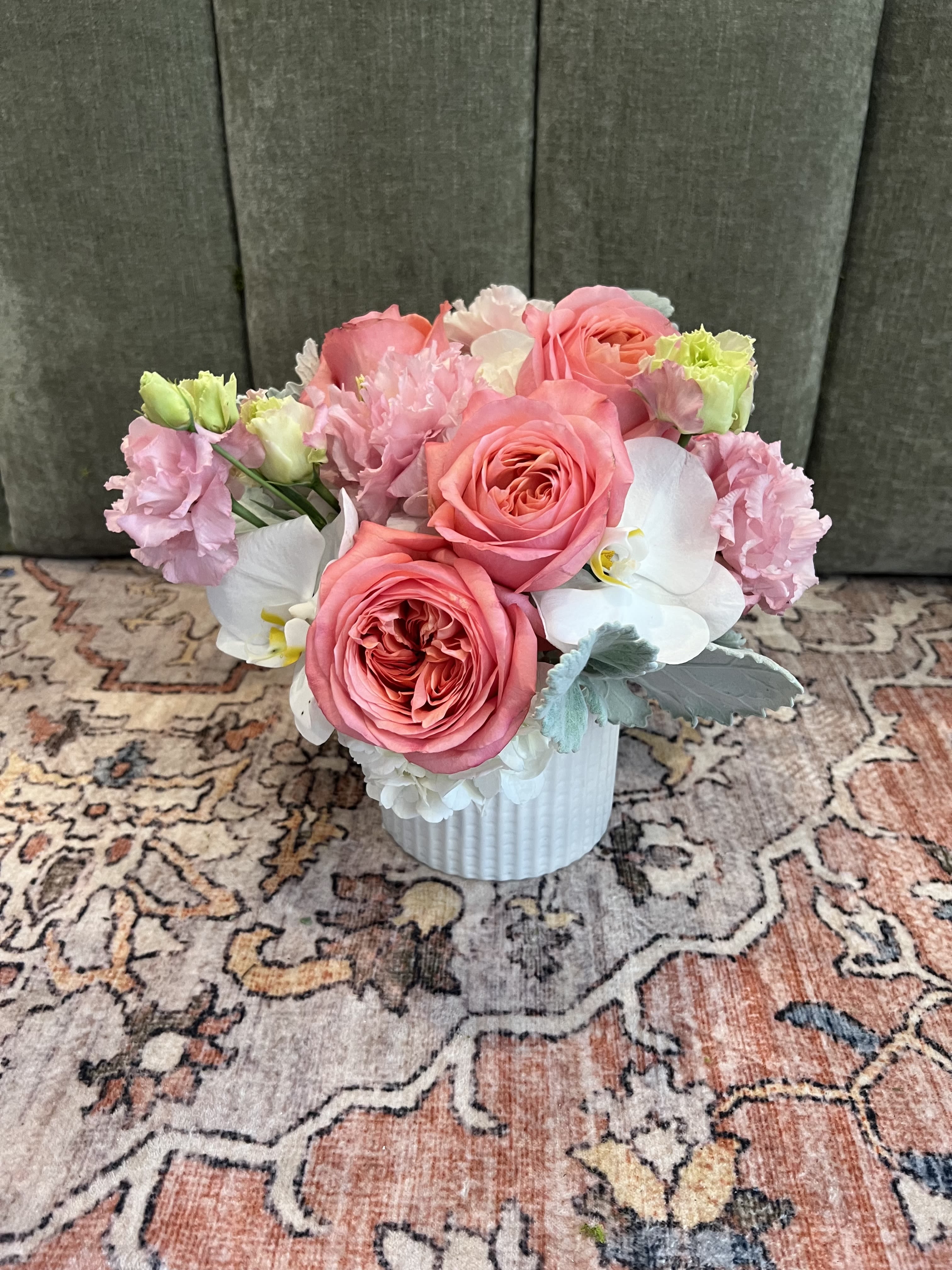 Pink Punch  - Coral-pink roses take center stage in this Pink Punch flower arrangement, surrounded by delicate white Phalaenopsis orchids and soft pink lisianthus to create a romantic, gently modern bouquet perfect for a birthday bouquet, anniversary flowers, or a thoughtful thank-you. The compact, rounded composition reads as polished and refined, the kind of gift that makes the person you're thinking of feel noticed and cherished.  Creamy hydrangea accents, pale green lisianthus buds, and muted blue‑gray foliage bring cool contrast to the warm pinks and whites, giving the design depth and a softly textured look. Flowers are presented in a white ribbed ceramic vase that enhances the arrangement's clean, contemporary style and makes it ready to display on a bedside table, desk, or dining centerpiece.  This arrangement is ideal for celebrating intimate moments or offering comfort without fuss-she'll feel genuinely celebrated whether it marks a milestone or simply brightens her day. The compact vase makes it easy to place and enjoy; change the water every few days and trim stems slightly to prolong freshness.