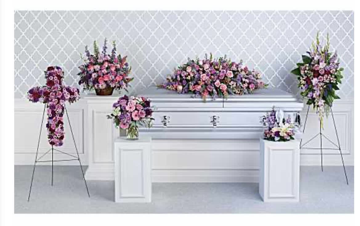 Beloved Collection Casket Package - Soft lavender, pink and white blooms arranged across a coordinated funeral set make a graceful tribute for a loved one. This flower arrangement collection for a casket and service brings together roses, carnations, lilies, daisies and complementary greenery to create upright sprays, a full casket spray, and smaller vase pieces-designed specifically for sympathy and memorial services to surround a white casket with a calm, comforting presence.  The designs feature layered textures and gentle color transitions from blush pink to deeper purple, with white accents to brighten the display. Pieces sit on white pedestal stands and a metal easel where needed, and the vases and spray mechanics are sized to balance proportionally around the casket; a glass vase is included for the smaller arrangements and the casket spray covers the lid with a lush, elongated profile. The overall composition reads formal yet tender, drawing the eye while allowing guests space to gather and remember.  Choose this coordinated casket package when you want the person you've lost to feel honored and gently celebrated-this set conveys sympathy, love, and peaceful reflection. Ordering includes placement-ready pieces appropriate for viewings and funeral services; contact us for delivery timing, cemetery/vigil coordination, or to adjust colors and scale to suit the service.
