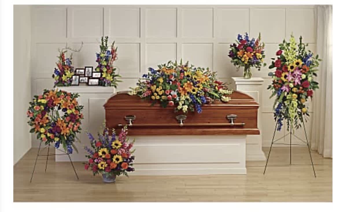 The Celebration of Life Collection Casket Package - A vivid, heartfelt tribute that brings color and warmth to a funeral setting, this flower arrangement is designed as a casket spray and accompanying standing pieces for a memorial or celebration of life. The arrangement type and occasion-funeral casket flowers for a celebration of life-are reflected in the bright mixed-color palette so your person is remembered with joy as well as reverence. The effect is both traditional and uplifting: dignified framing with lively hues that soften a solemn moment and honor a life well lived.  Dense clusters of daisies, carnations, chrysanthemums, delphinium, roses and complementary seasonal blooms create a rich tapestry of red, yellow, blue, pink and purple across the display. A large, formal casket spray drapes across the polished wooden casket while matching standing sprays on easels and pedestal stands provide graceful vertical presence around the casket. Arrangements are finished with classic styling on neutral white platforms to keep the focus on the flowers' textures and colors.  Perfect for families seeking a celebratory yet respectful presentation, this collection is intended to make the person you're honoring feel remembered and cherished. Our team will coordinate delivery and placement with the venue; sizes and exact bloom mix may vary slightly with seasonal availability to ensure freshness and the most vibrant presentation.