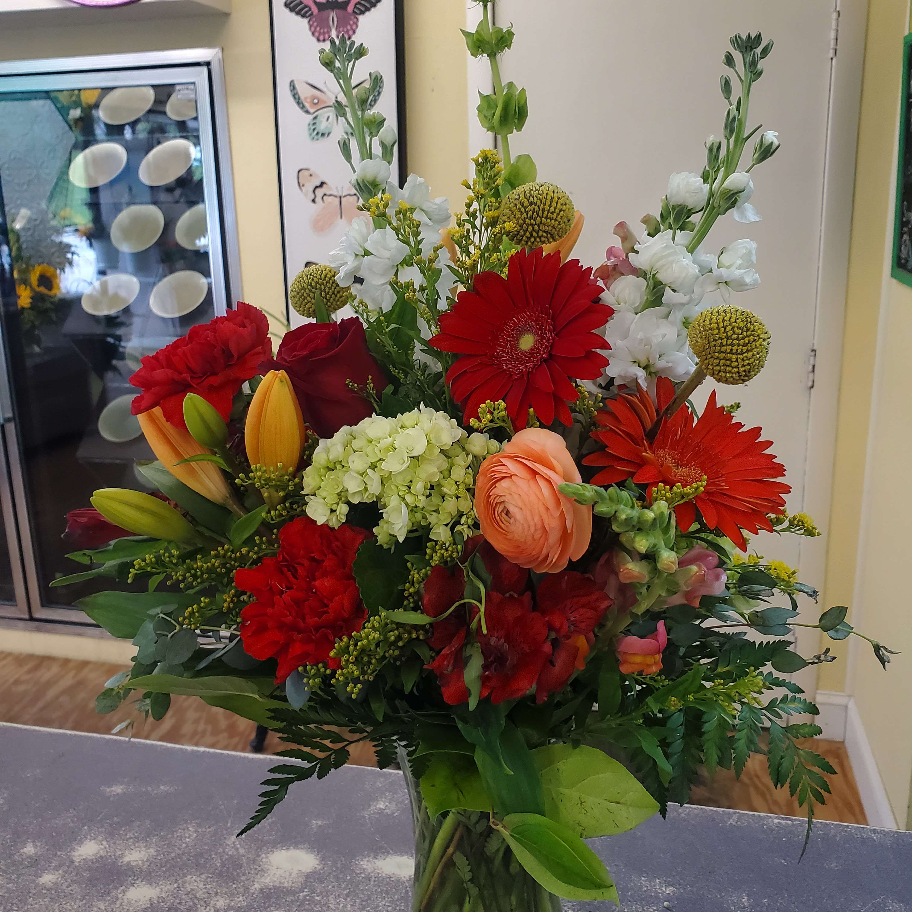 Mixed bouquet with red gerbera daisies, lilies, and white flowers in a glass vase
