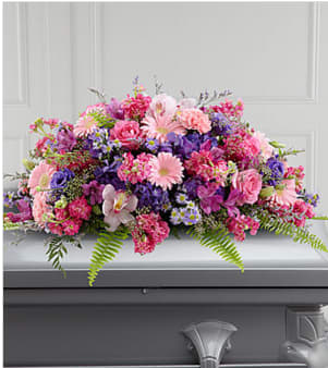 Glorious Garden Casket Cover (BB) - Create a tender and enchanting farewell tribute with our casket spray cover adorned with pink gerbera daisies, pink stock, pink roses, purple lisianthus, lush greenery, and delicate filler flowers. This captivating arrangement evokes a sense of grace, beauty, and remembrance, serving as a touching and heartfelt tribute to your beloved.