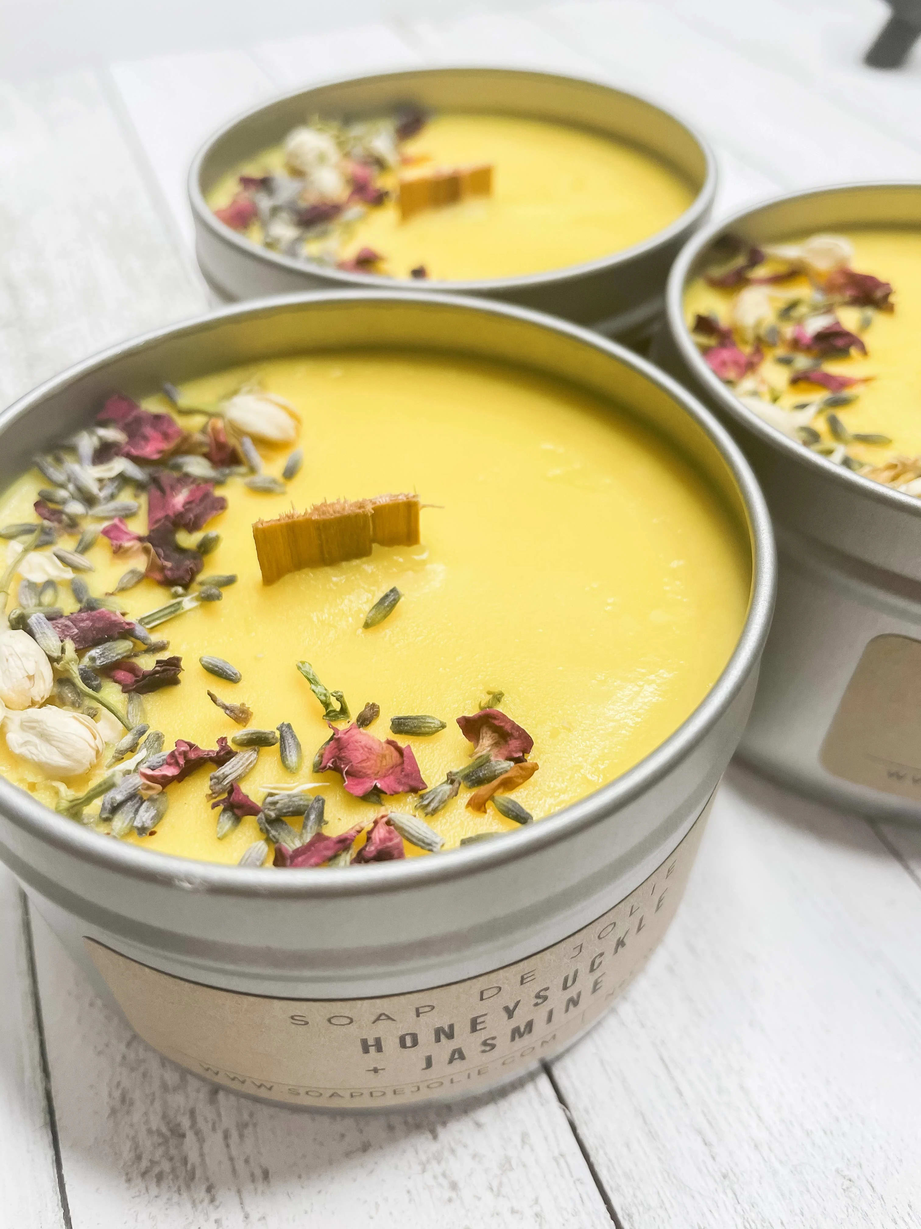 Three yellow candles in round tins topped with dried flower petals
