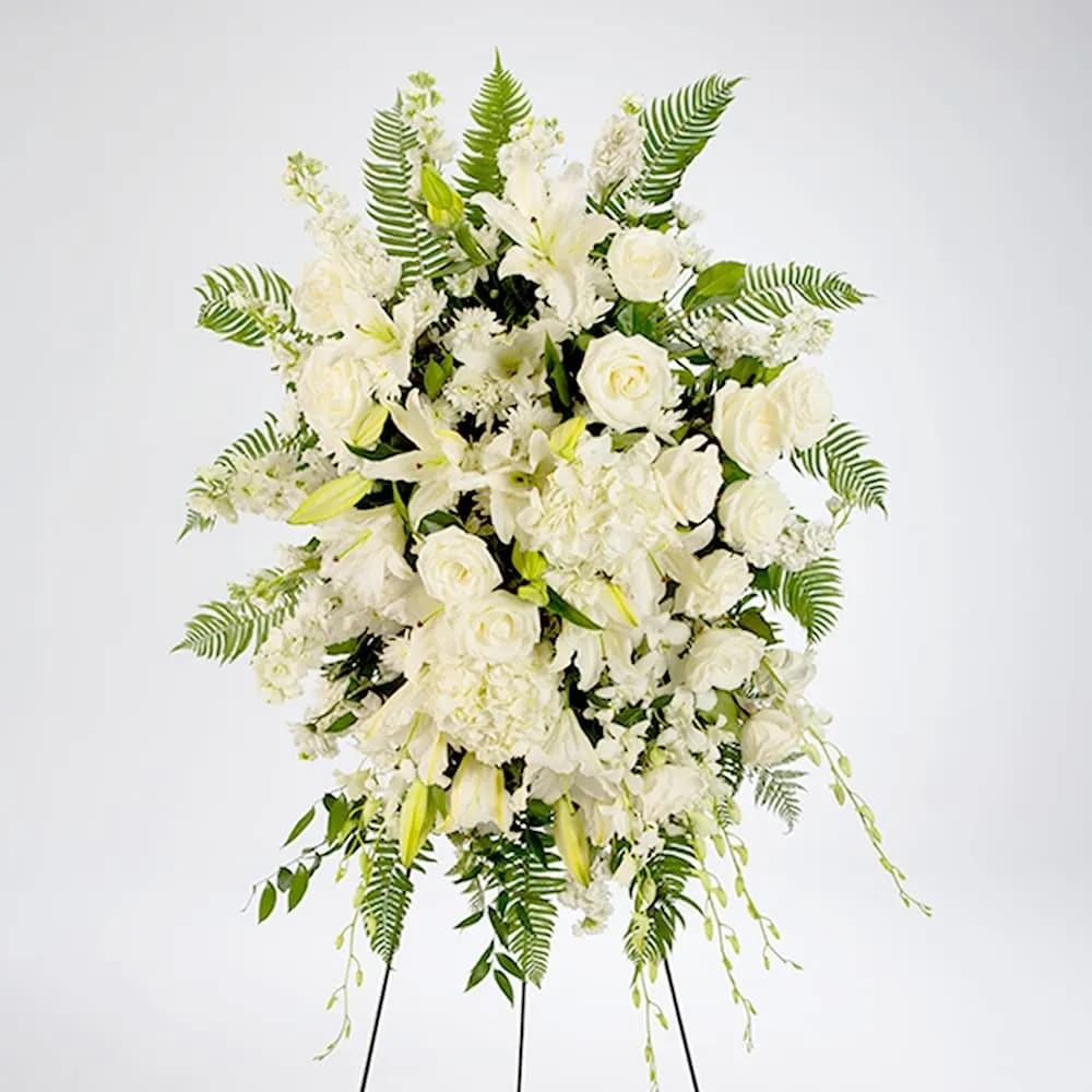 True Sympathy (BB) - Create a serene and elegant atmosphere at your loved one's service with our exquisite all-white standing spray. This stunning arrangement combines the timeless beauty of white roses, stock, hydrangea, dendrobium orchids, and lilies, coming together to form a breathtaking tribute of purity, love, and serenity.