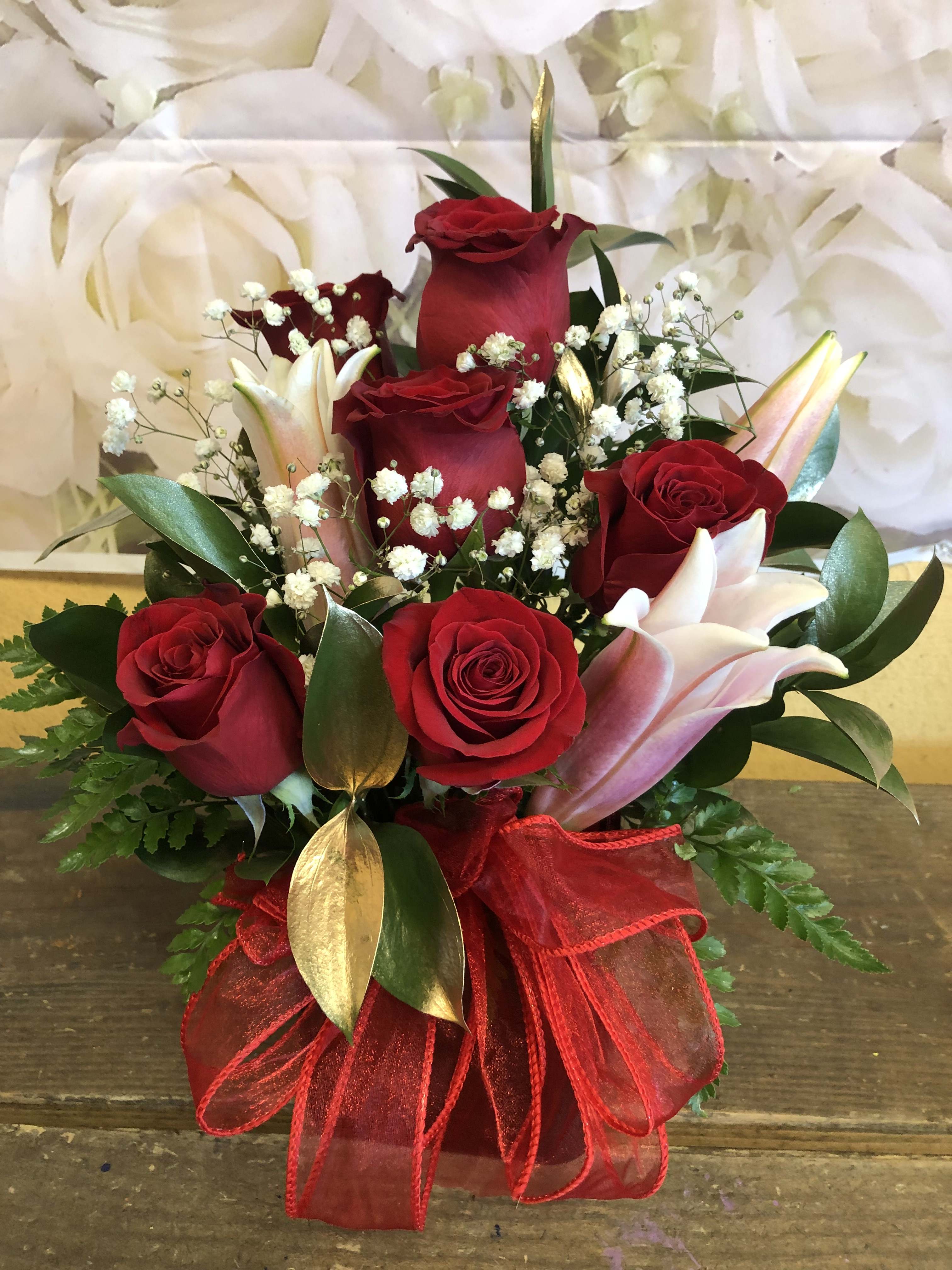 Red roses and pink lilies arranged with baby's breath in a red ribbon wrap