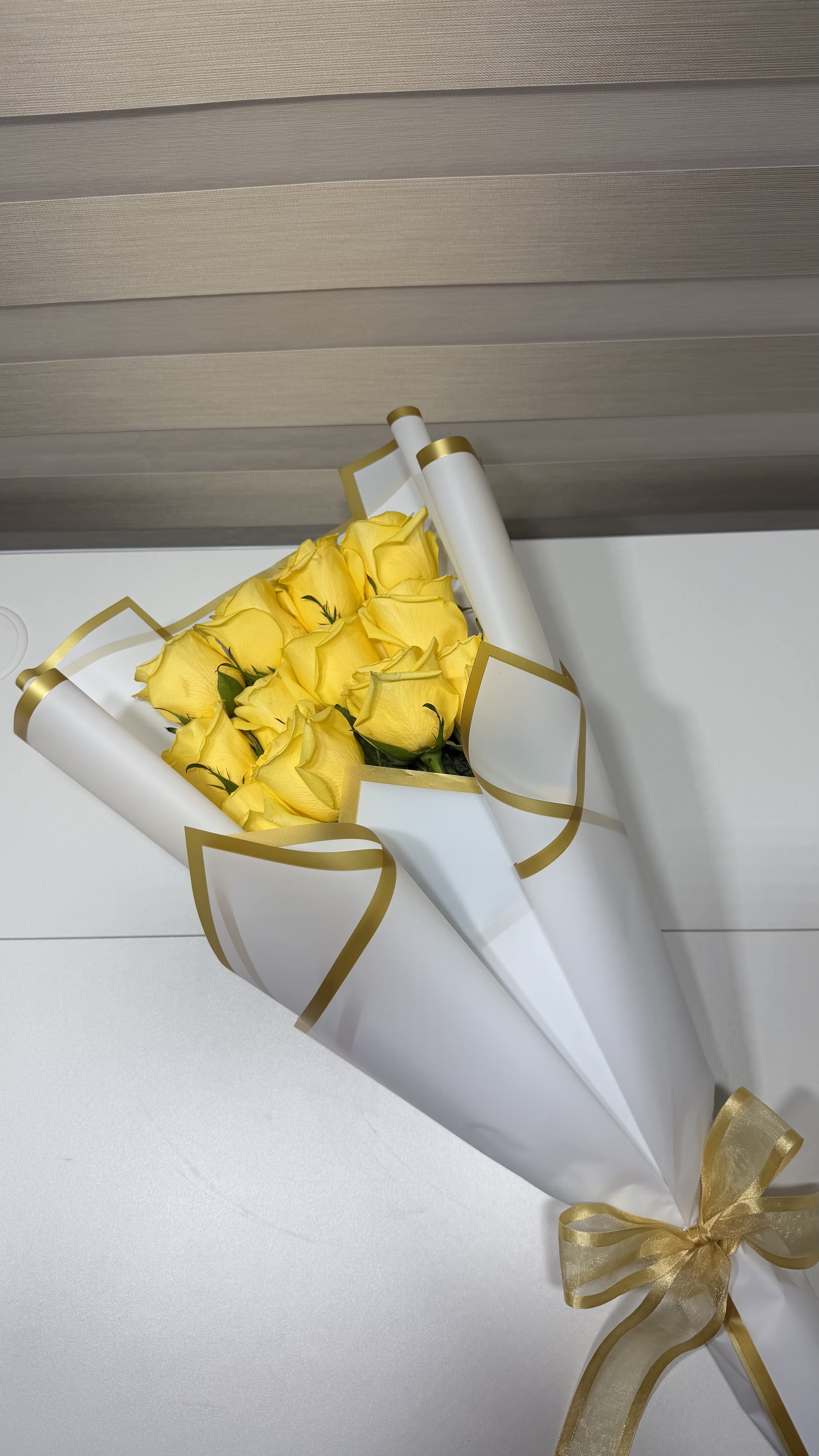 Bouquet of yellow roses wrapped in white paper with gold trim