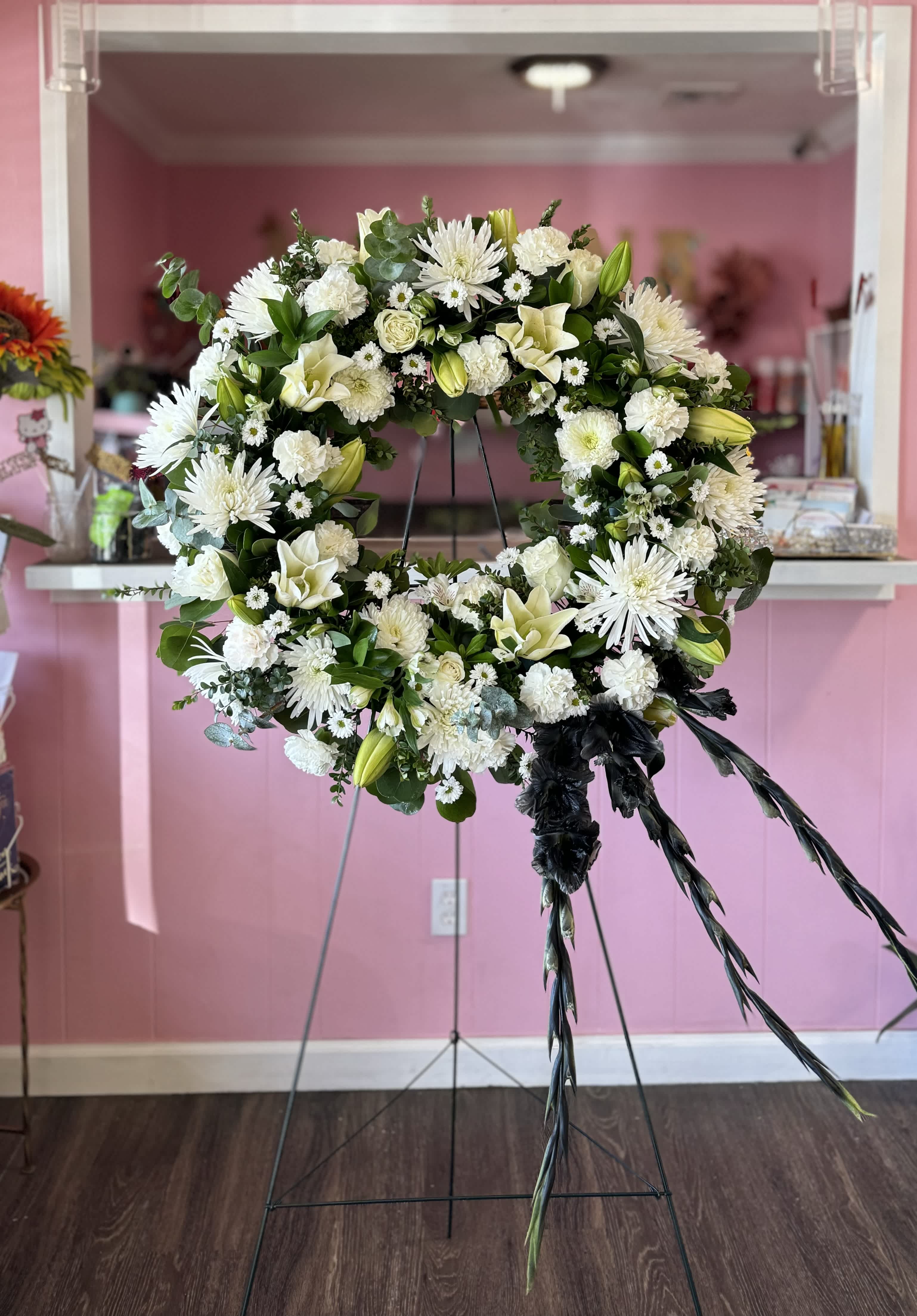White floral wreath on a stand with black ribbon streamers