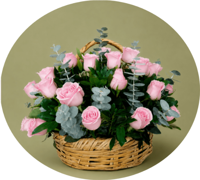 PINK KANASTA - A dense cluster of pale pink roses arranged low in a woven basket creates an immediately romantic, garden-like impression - perfect as an anniversary bouquet, a Mother's Day gift, or a thoughtful just-because surprise. Silvery eucalyptus stems rise through the soft pink blooms, their cool-toned contrast and dark green foliage giving the arrangement a fresh, hand-gathered look that reads both elegant and gently rustic.  The low, rounded composition feels full and abundant without being fussy: pale pink roses surrounded by eucalyptus in a warm woven basket with a handle for easy carrying and display. Sized to sit beautifully on a dining table or bedside table, the piece sends a clear message of affection and quiet celebration - she'll feel truly seen when this arrives on her doorstep.
