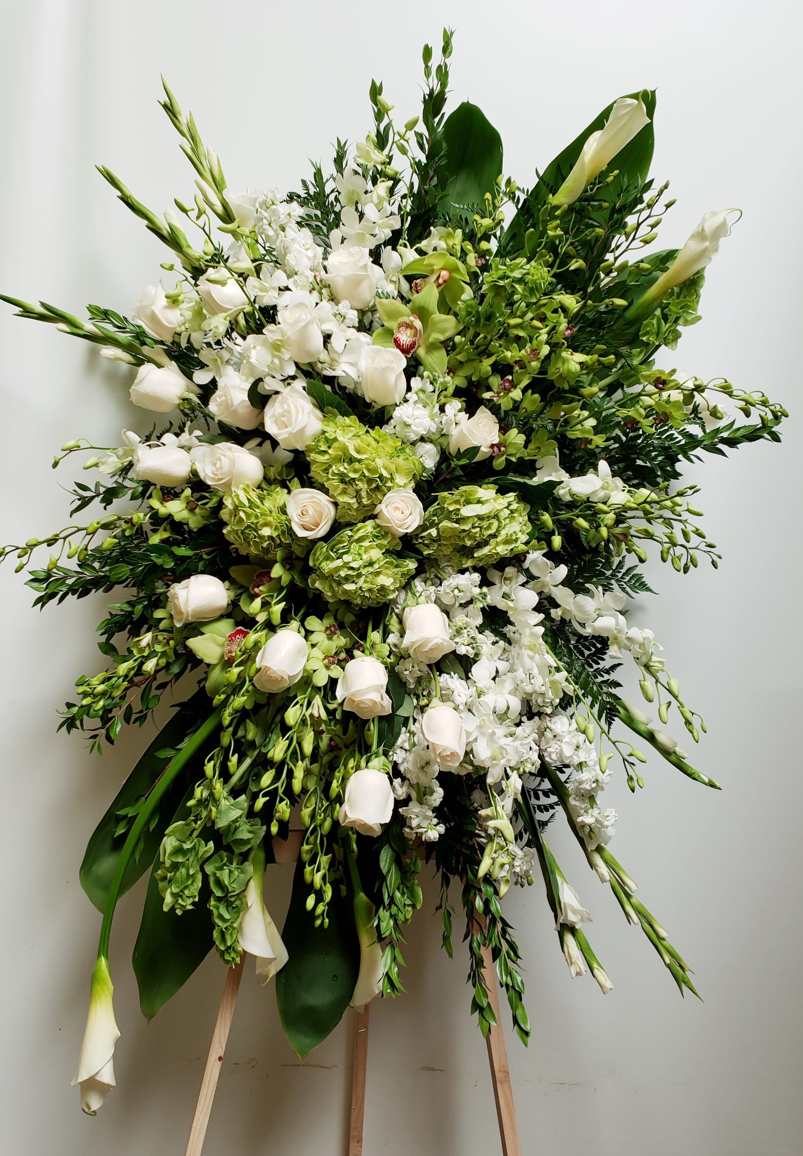 Large white and green funeral spray with roses and orchids on a stand