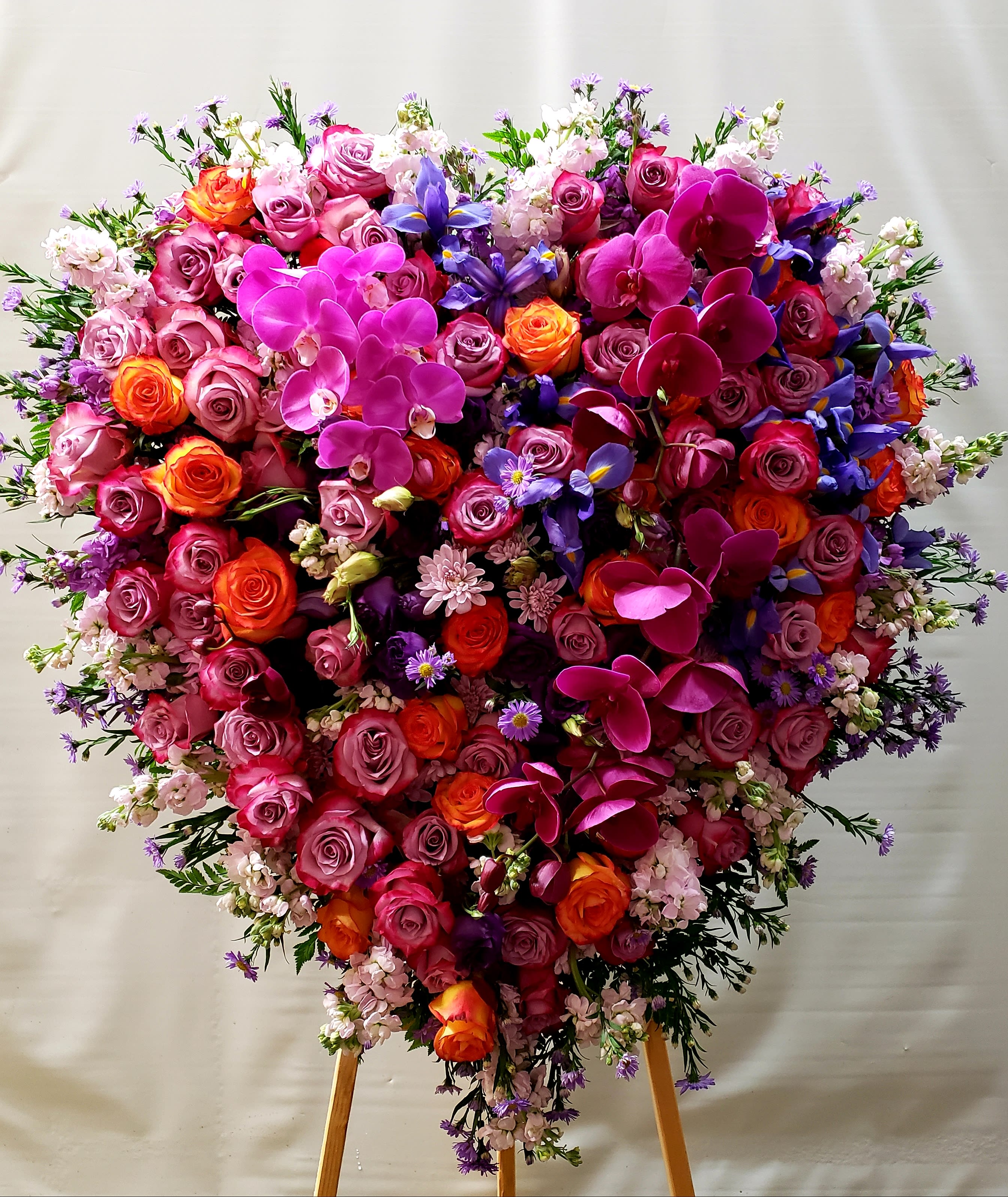 Heart-shaped floral arrangement with pink roses, orchids, and purple flowers