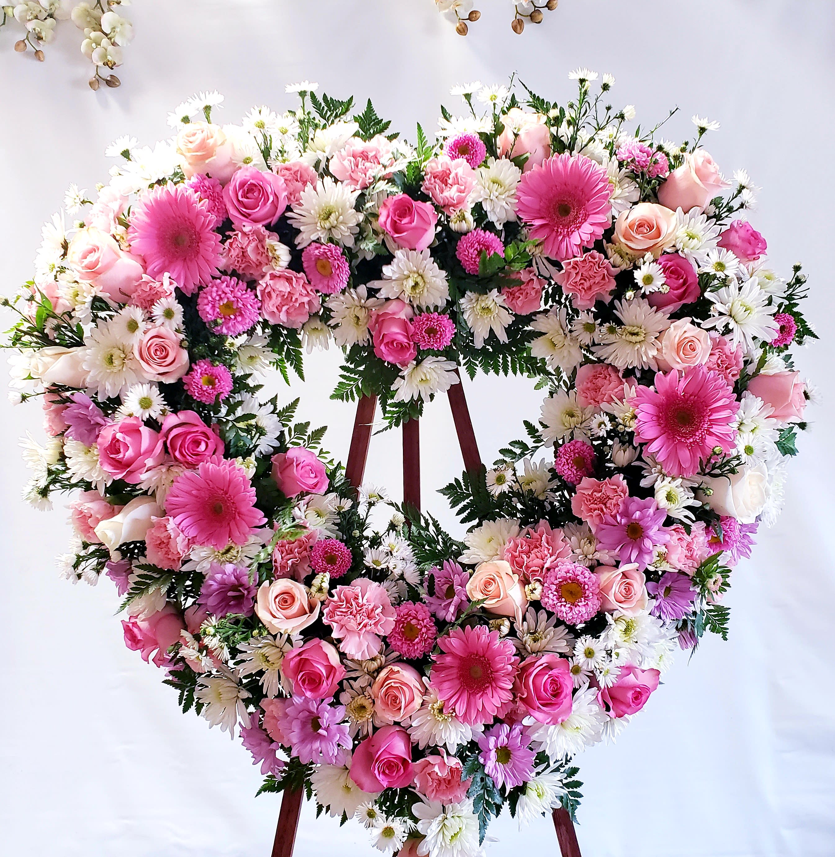 Heart-shaped floral wreath with pink roses and white daisies on an easel