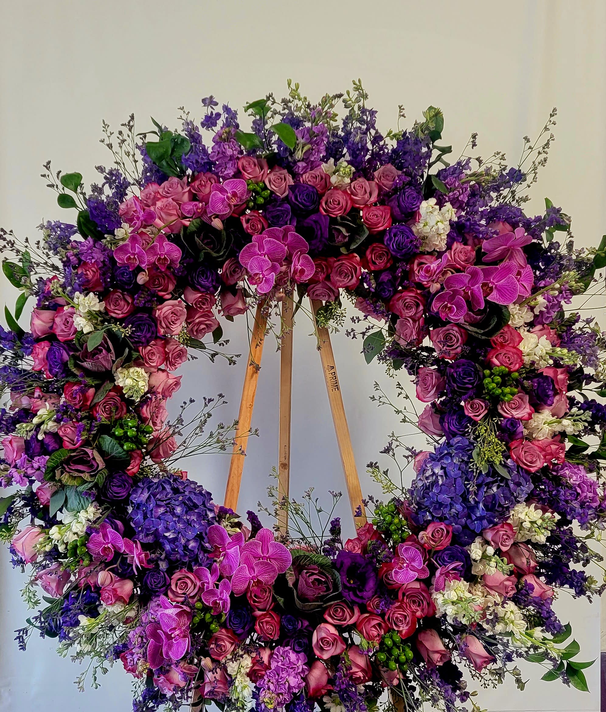Large floral wreath with pink, purple, and white blooms on a wooden stand