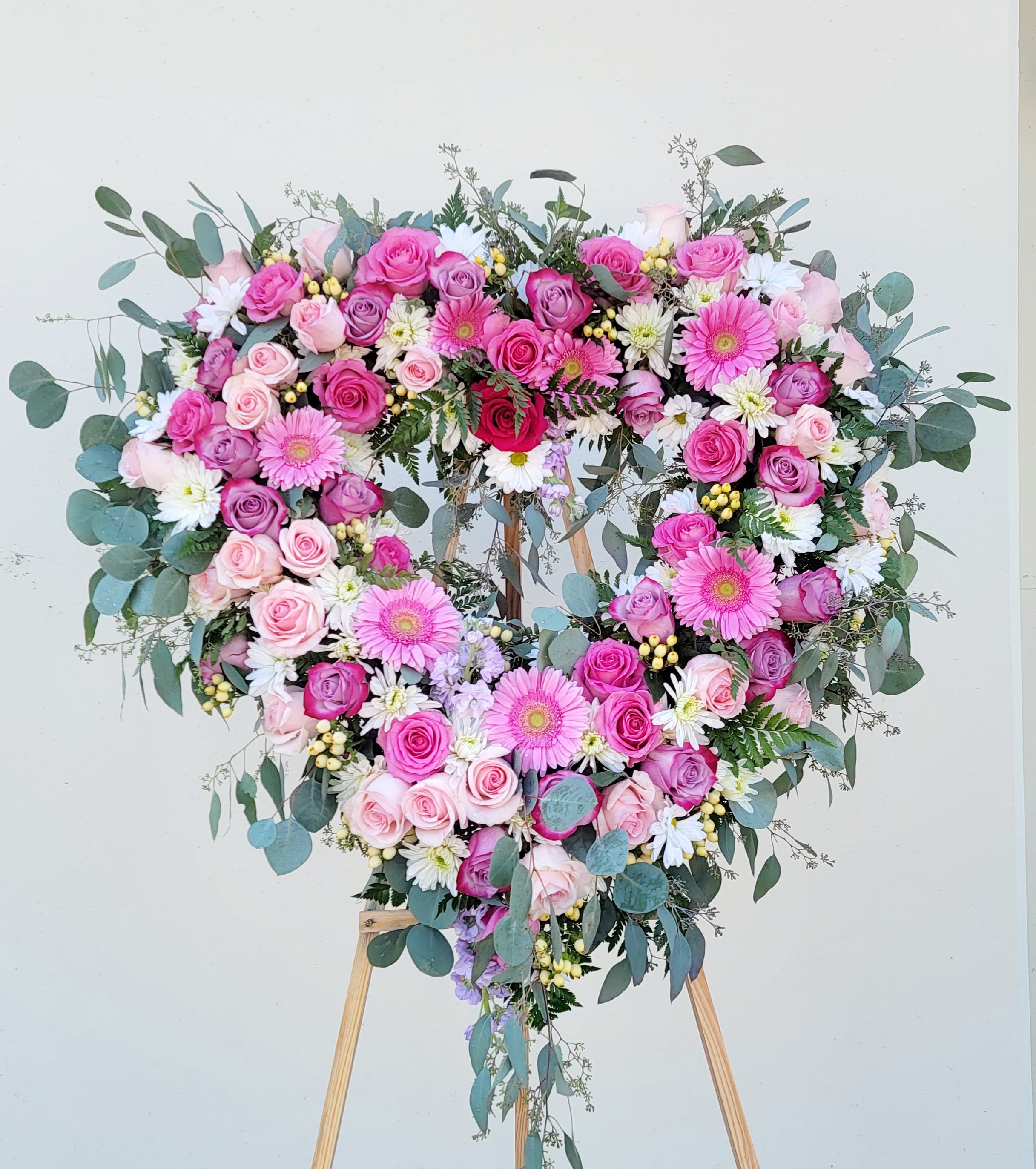 Heart-shaped floral wreath of pink roses and daisies on a wooden stand