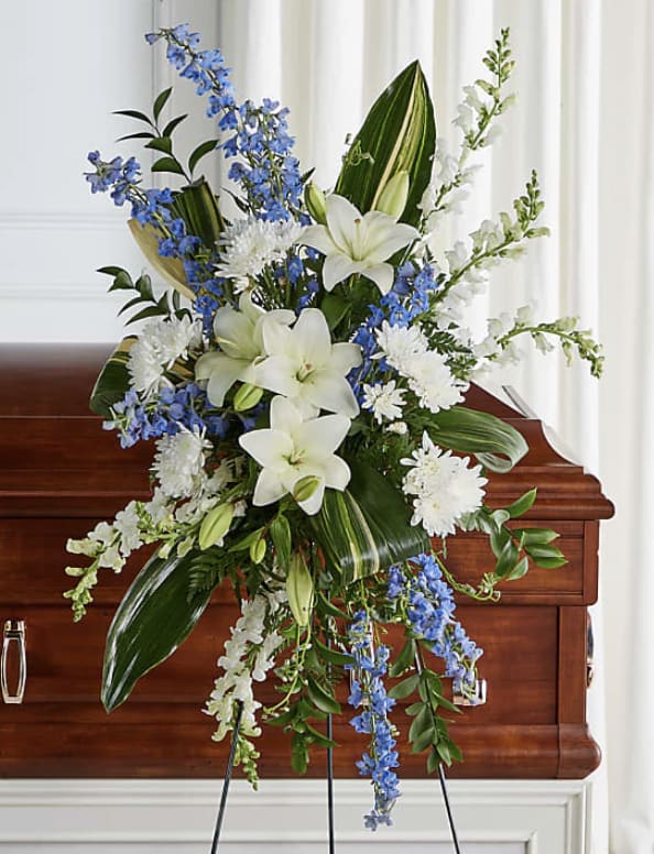 White lilies and blue flowers arranged on a wooden casket