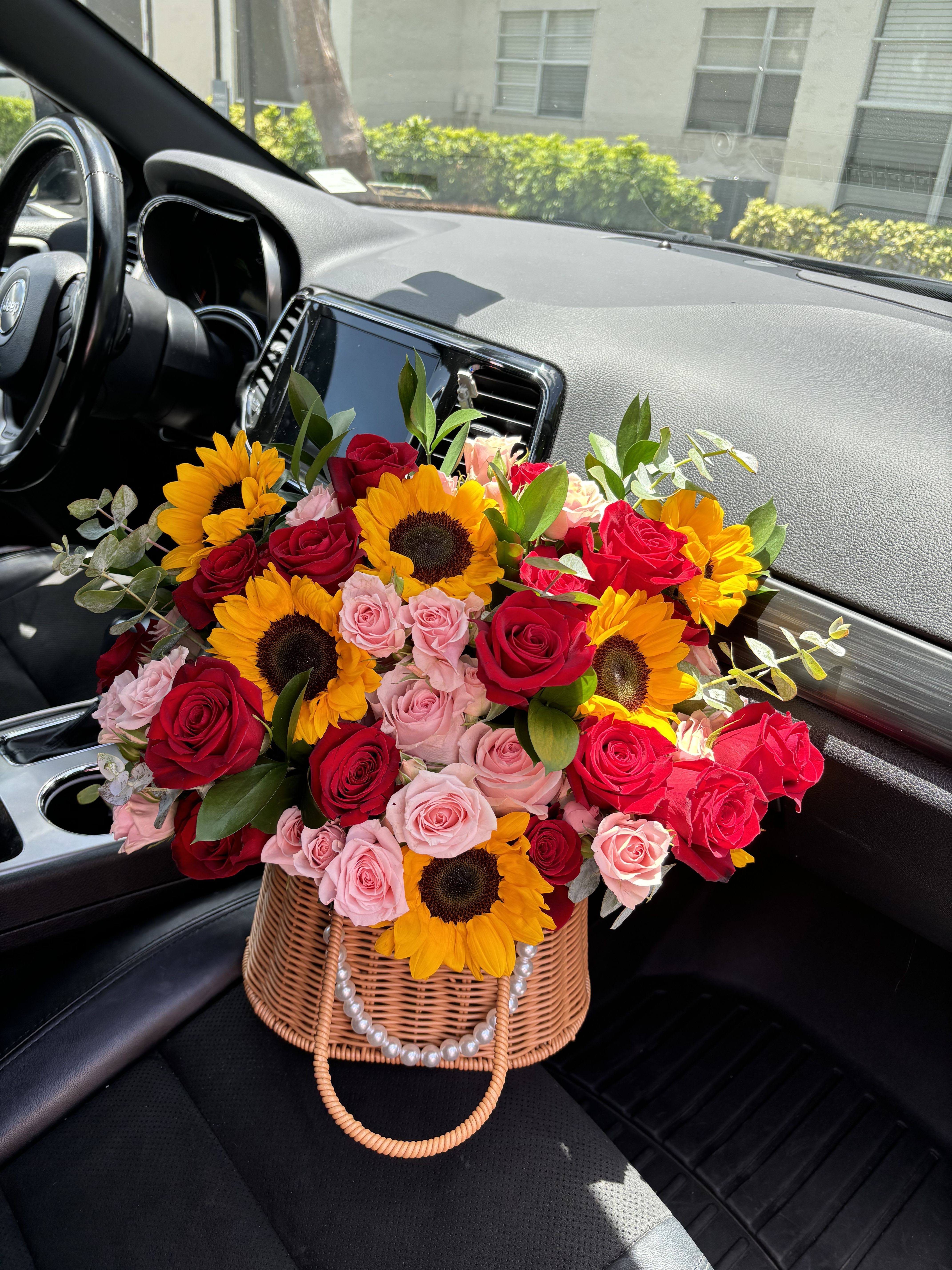 Basket arrangement of red and pink roses with sunflowers in a car seat