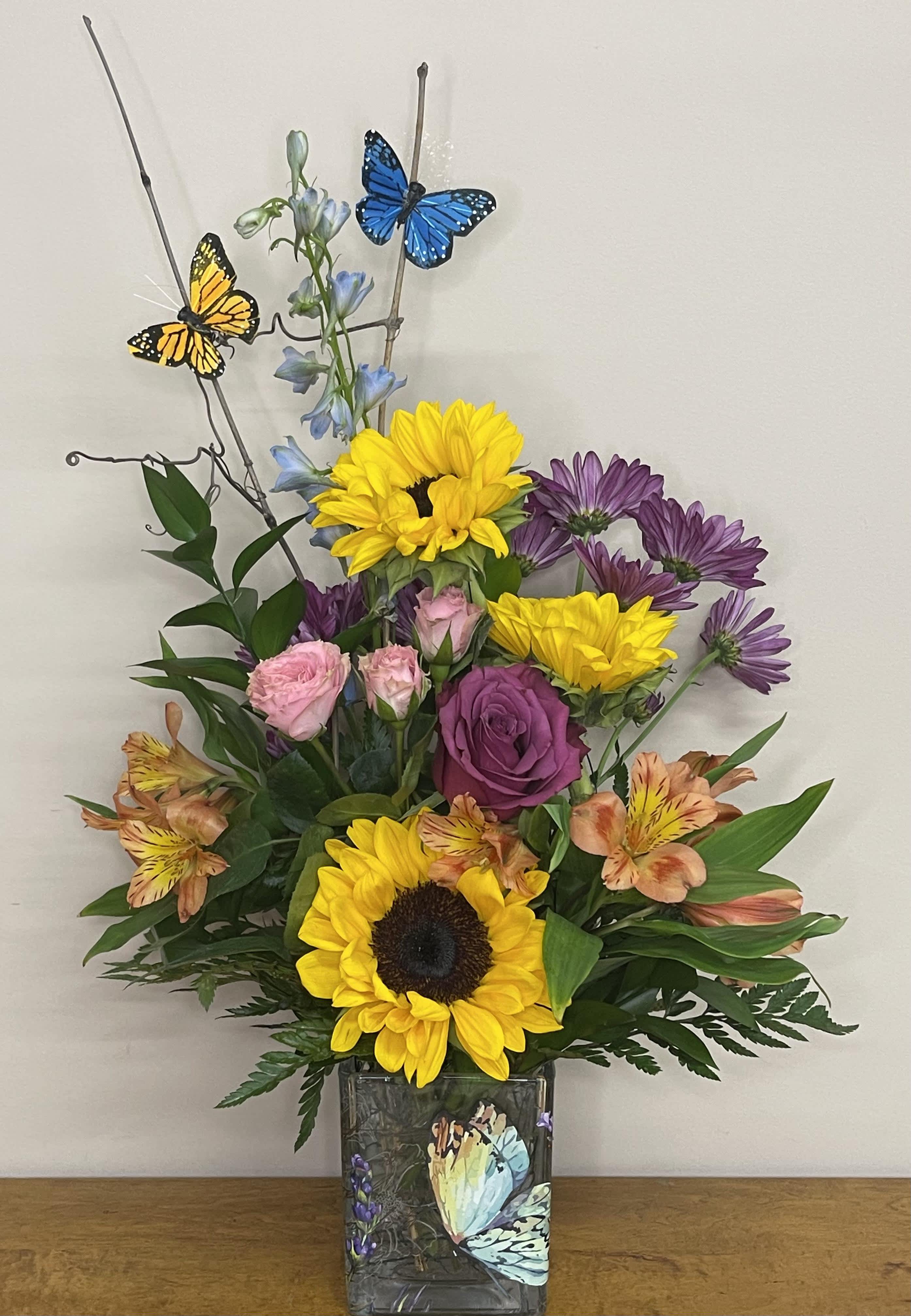 Mixed bouquet in a square glass vase with sunflowers, roses, and butterflies