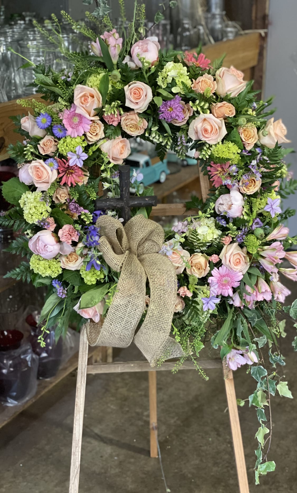 Floral wreath with pastel roses, daisies, and a burlap bow on an easel
