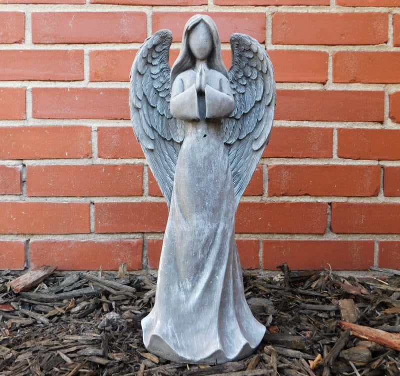 Gray angel statue with folded hands against a brick wall