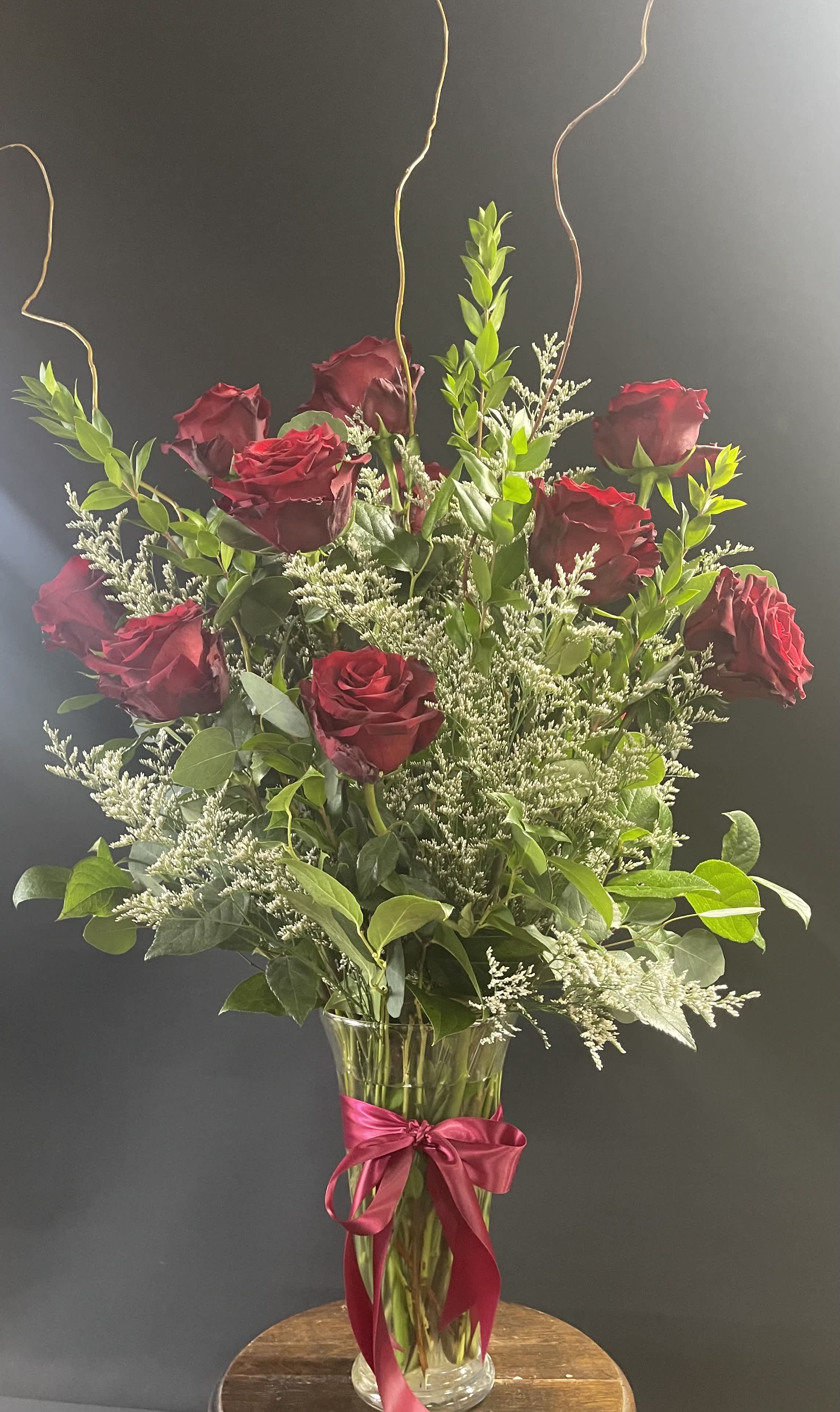 Red roses in a clear glass vase with a pink ribbon