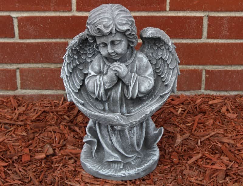 Gray angel statue with folded hands in front of a brick wall