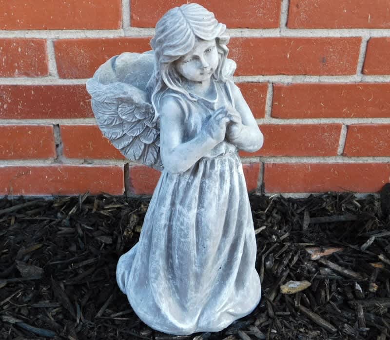 Small angel statue in a dress against a brick wall