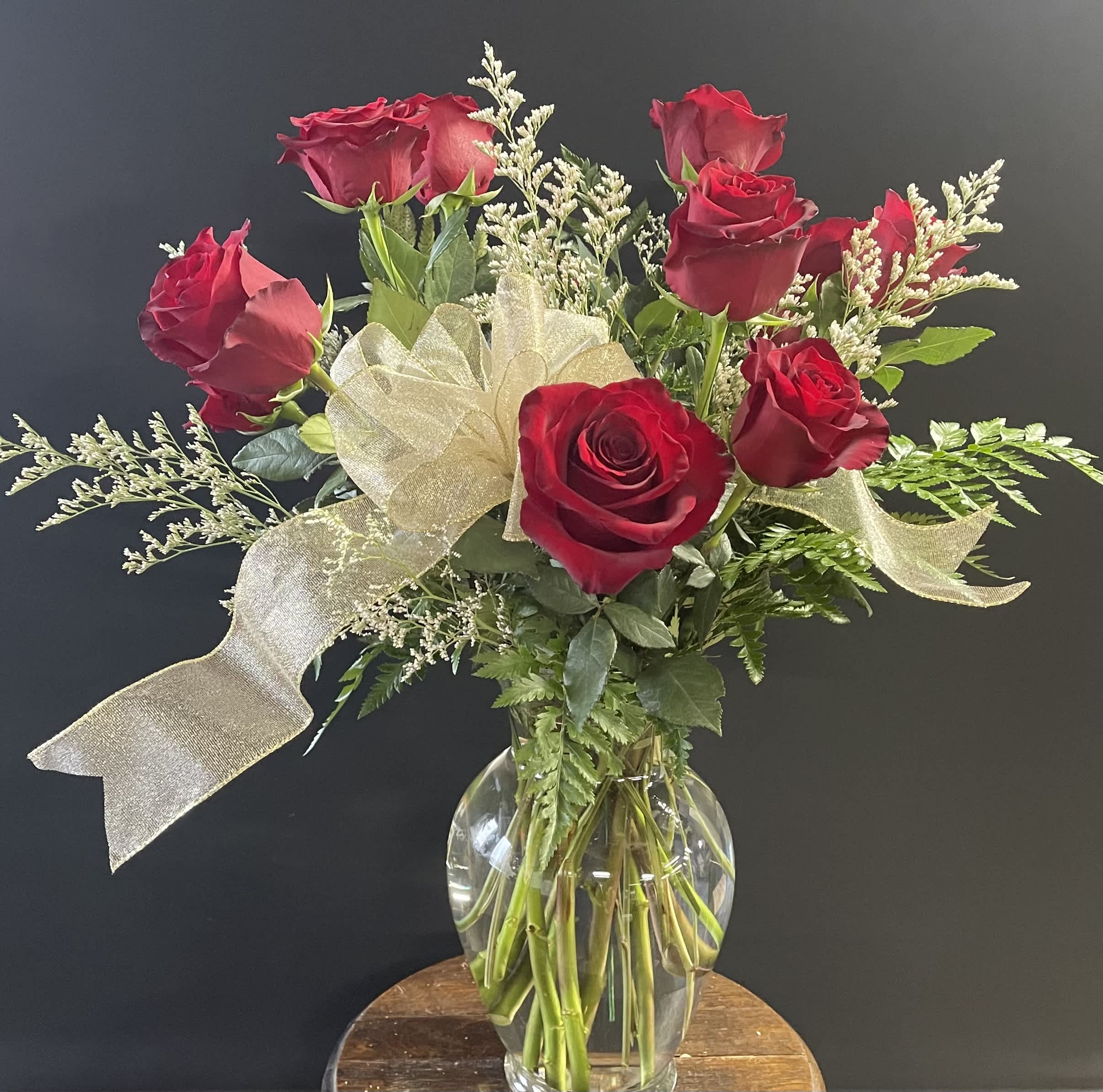 Red roses arranged in a clear glass vase with a gold ribbon