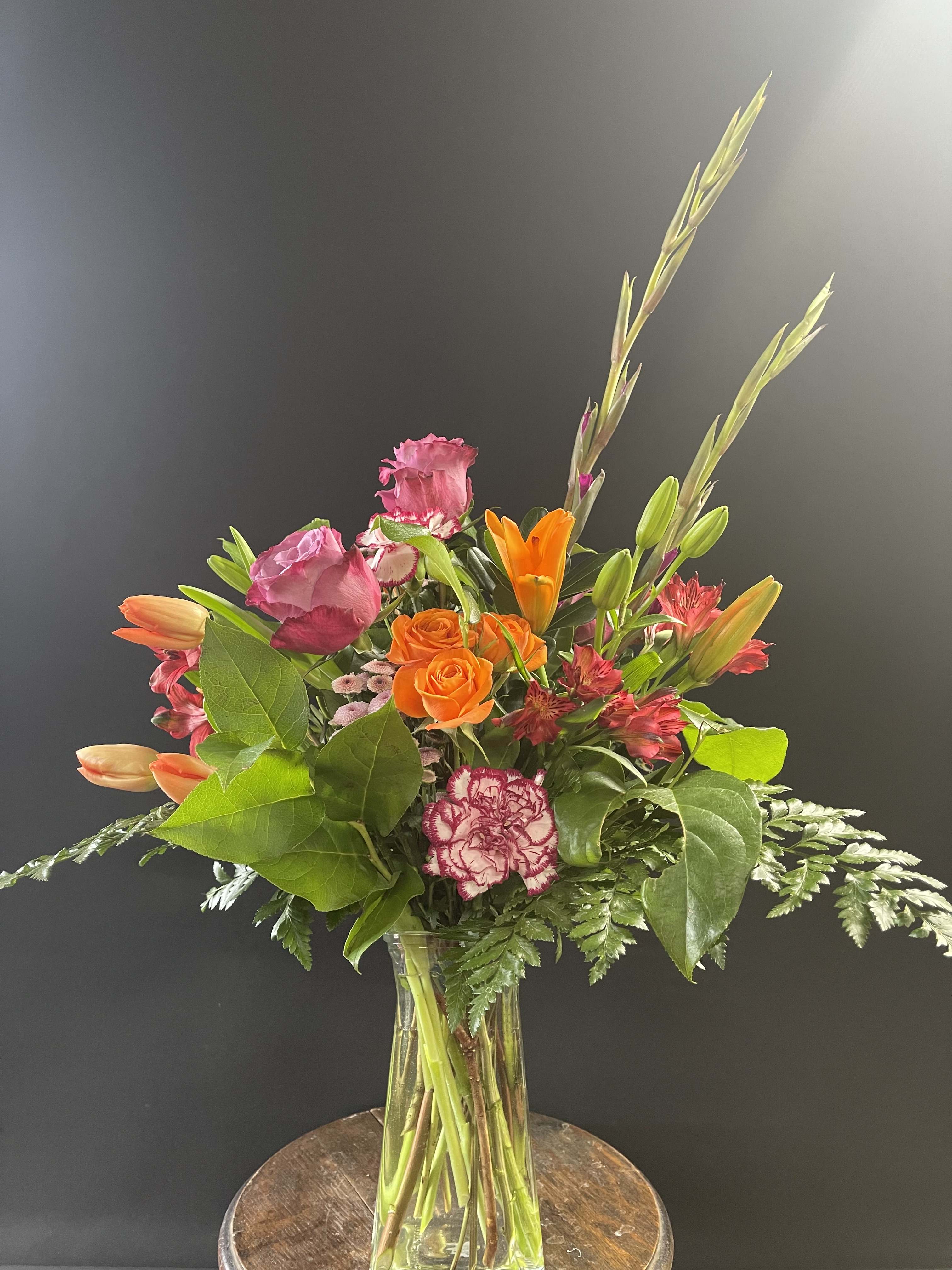 Mixed bouquet of orange and pink flowers in a clear glass vase