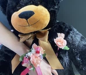 Black teddy bear with a gold bow and pink floral wrist corsage