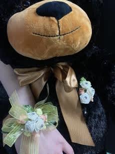 Black teddy bear with a gold bow and floral wrist corsage