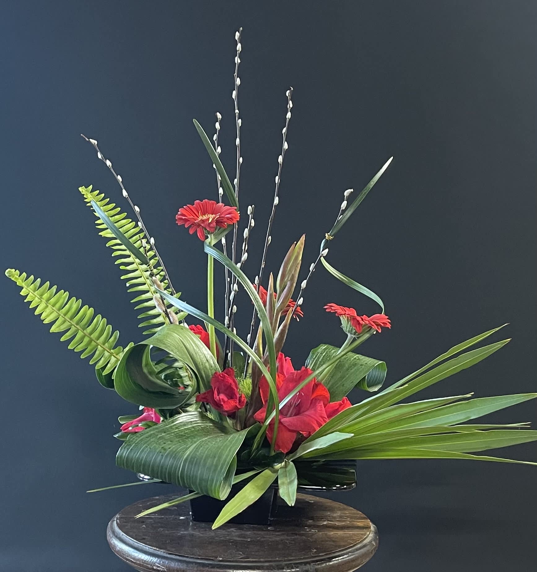 Red gerbera daisies in a black container with tall willow branches