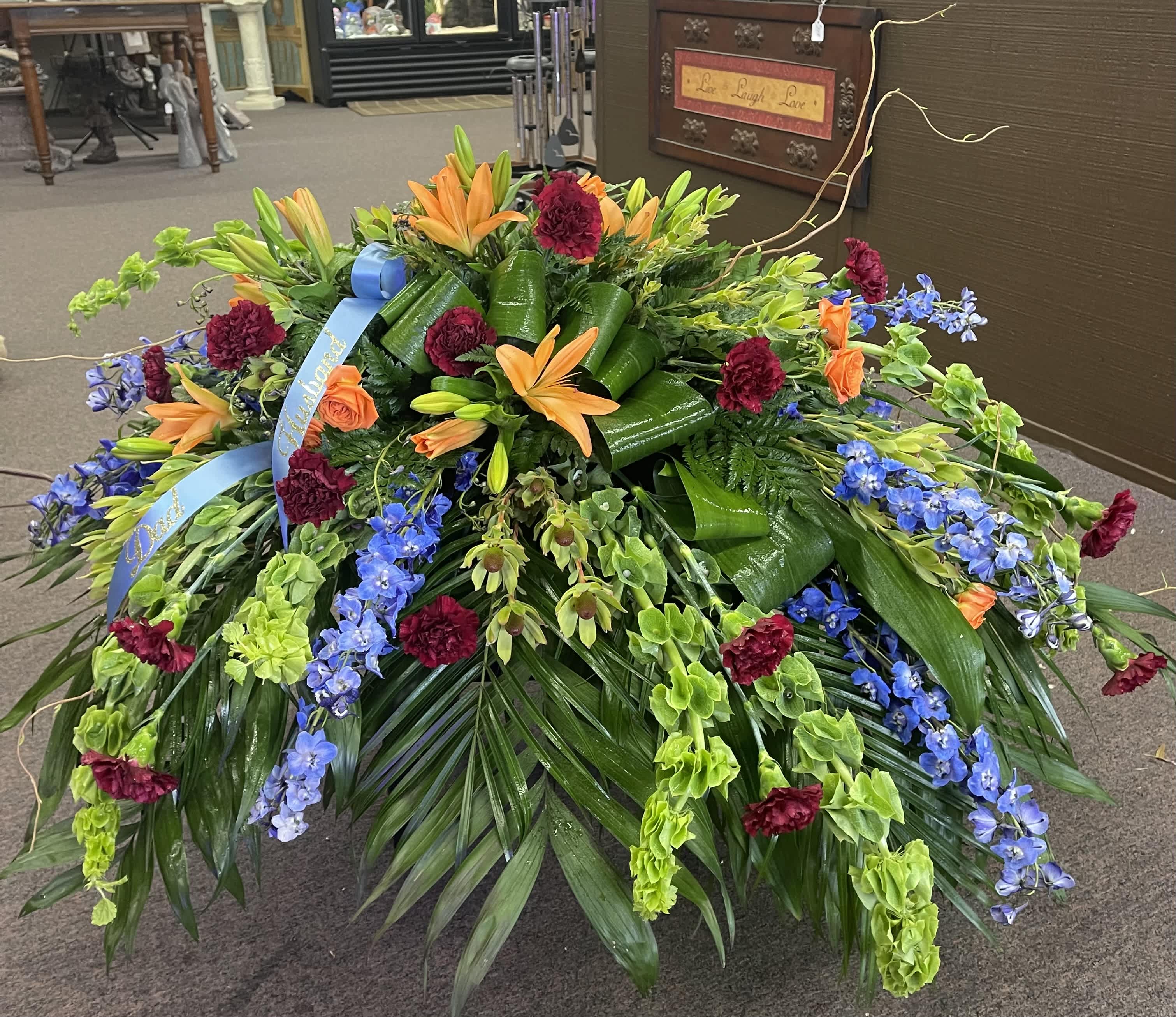 Large floral spray with orange lilies, blue flowers, and burgundy carnations