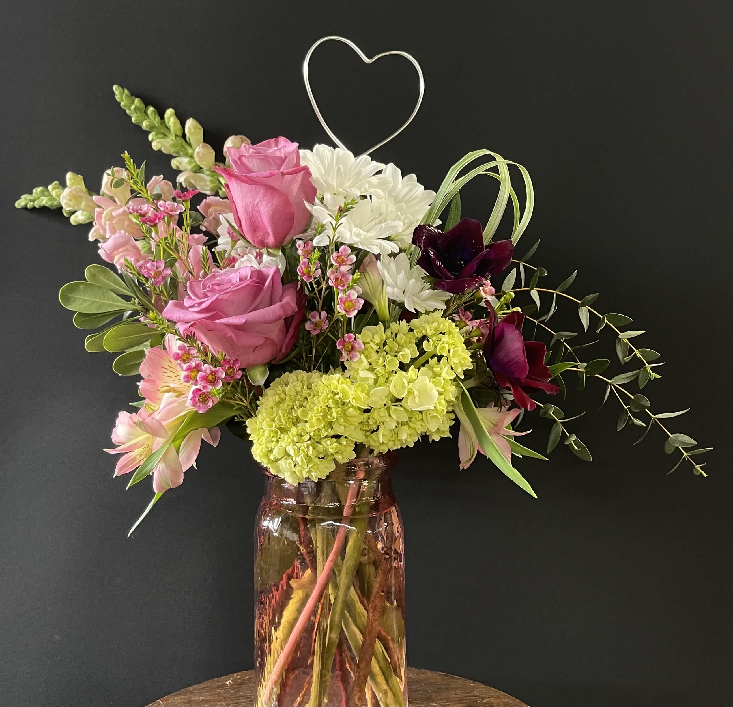 Mixed bouquet of pink roses, white daisies, and dark orchids in a glass vase