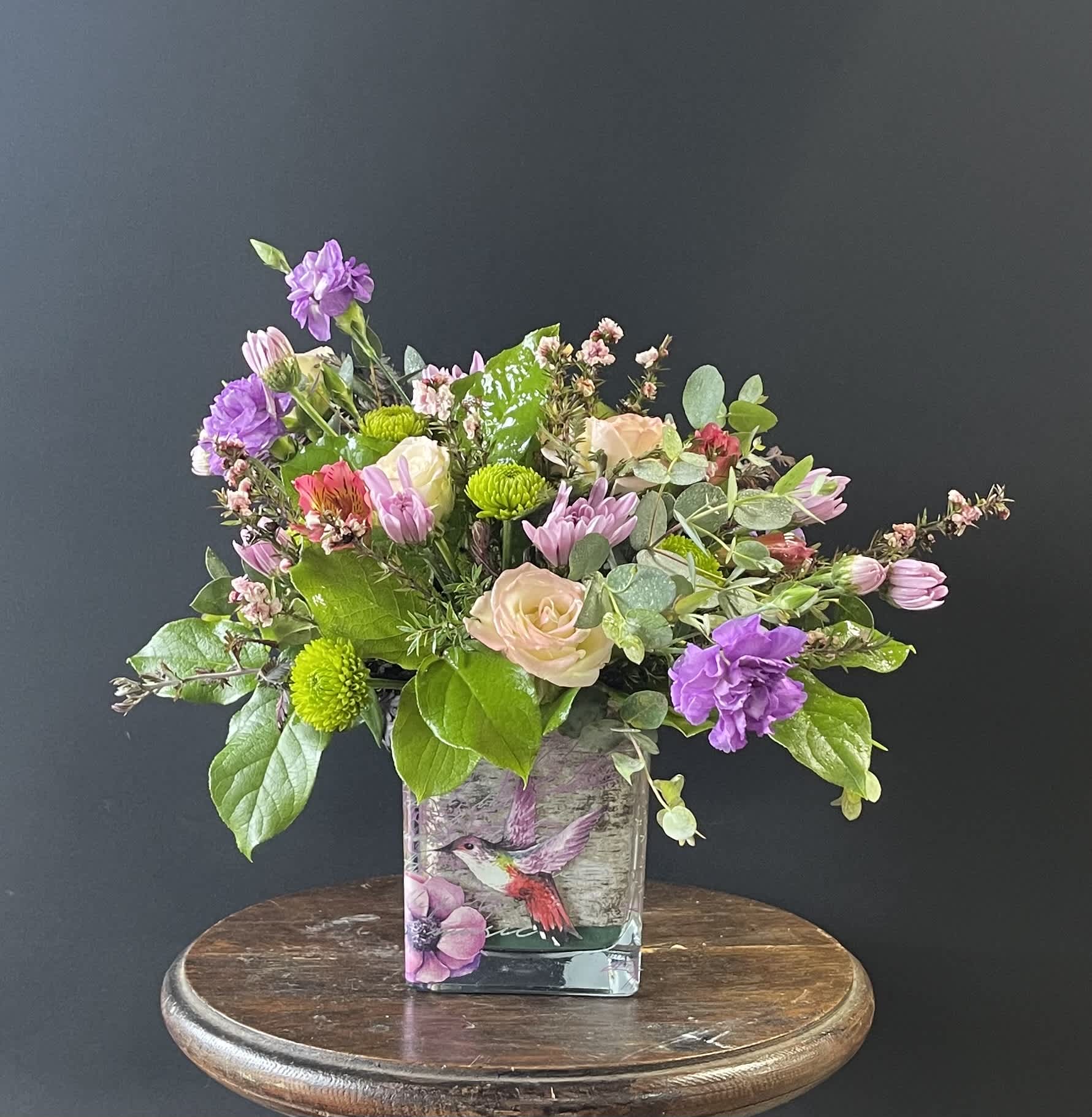 Mixed bouquet in a square glass vase with purple, pink, and green blooms
