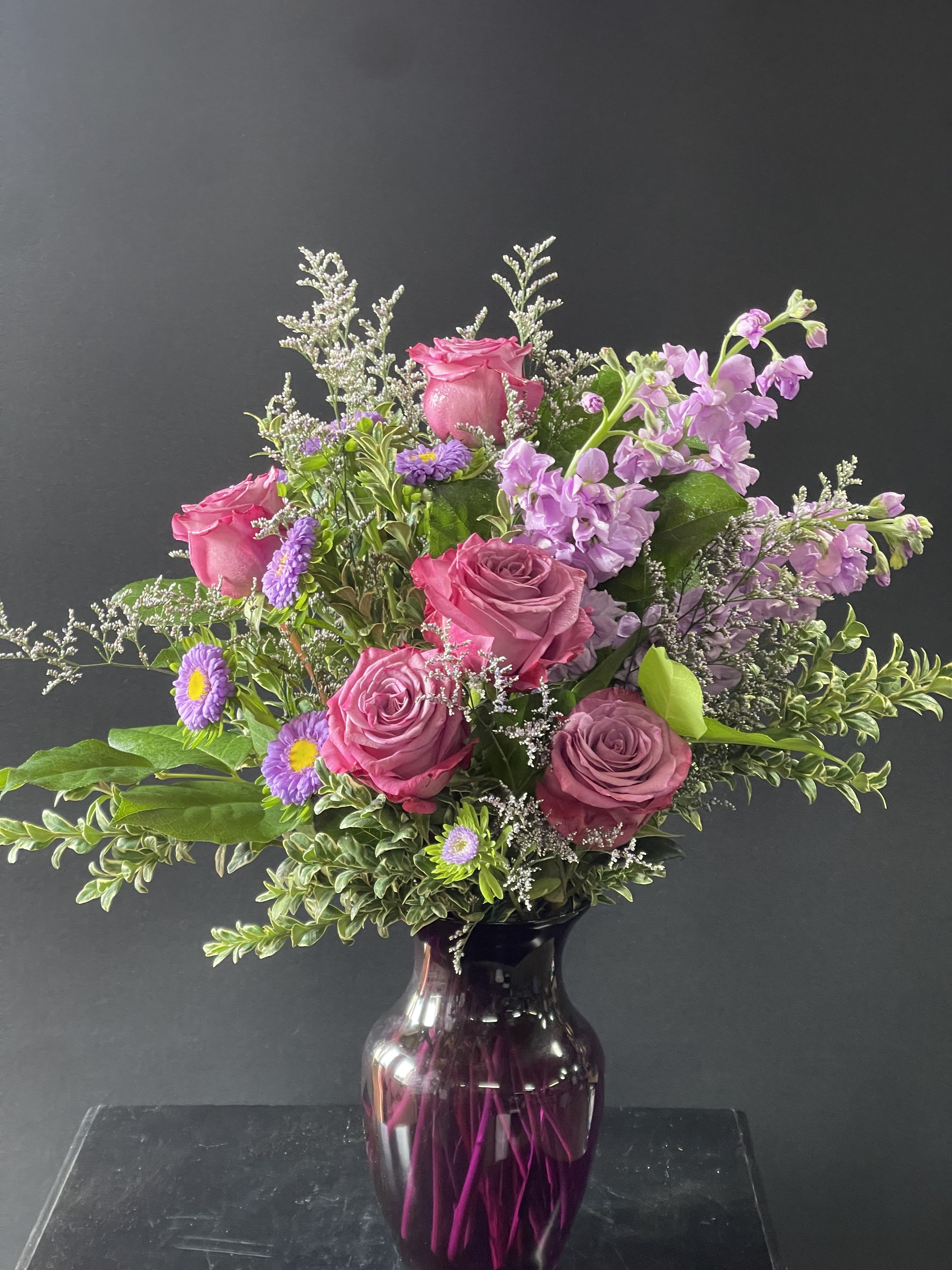 Pink roses and purple flowers in a dark glass vase