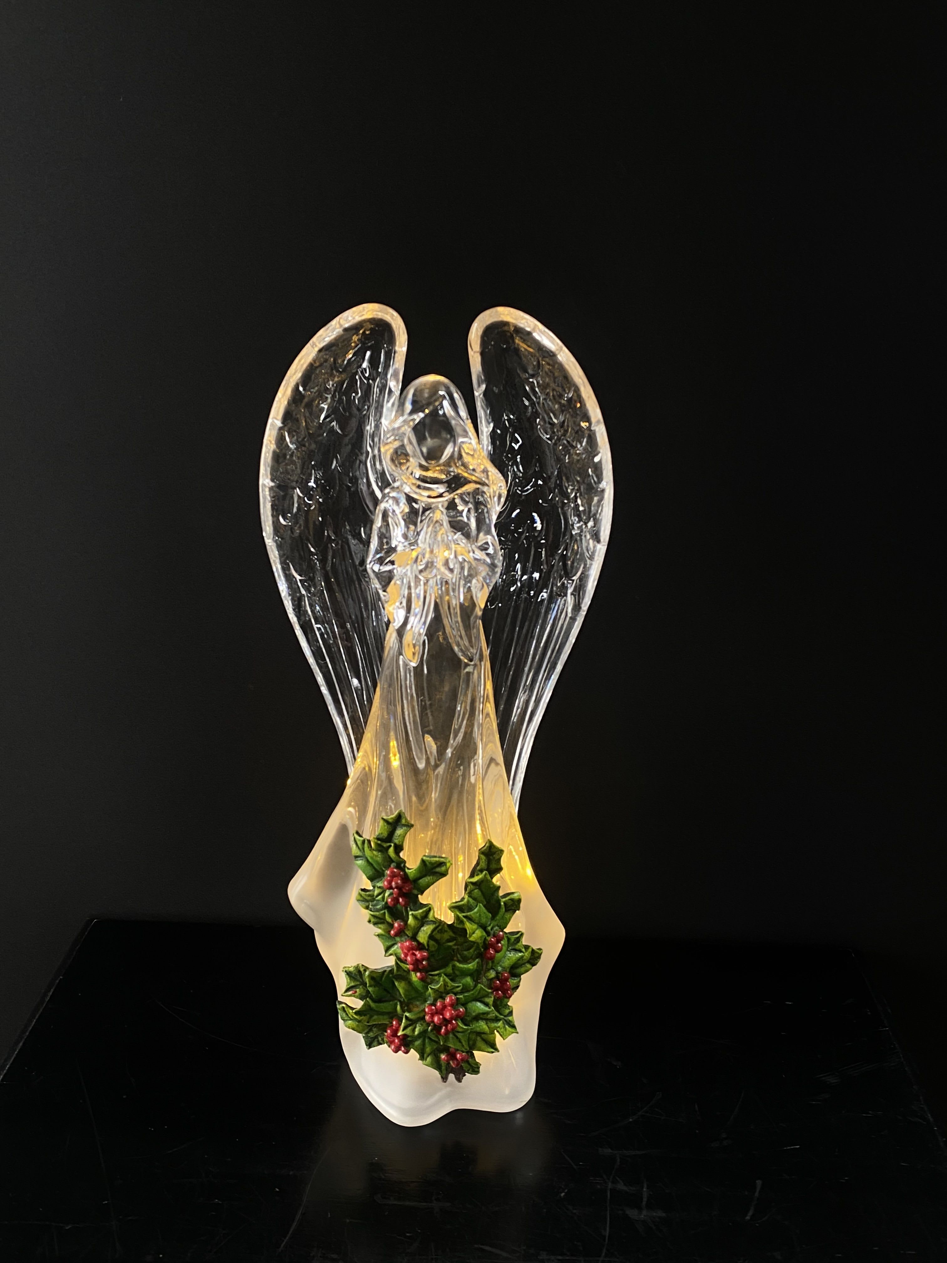 Glass angel figurine with holly decoration on a black background