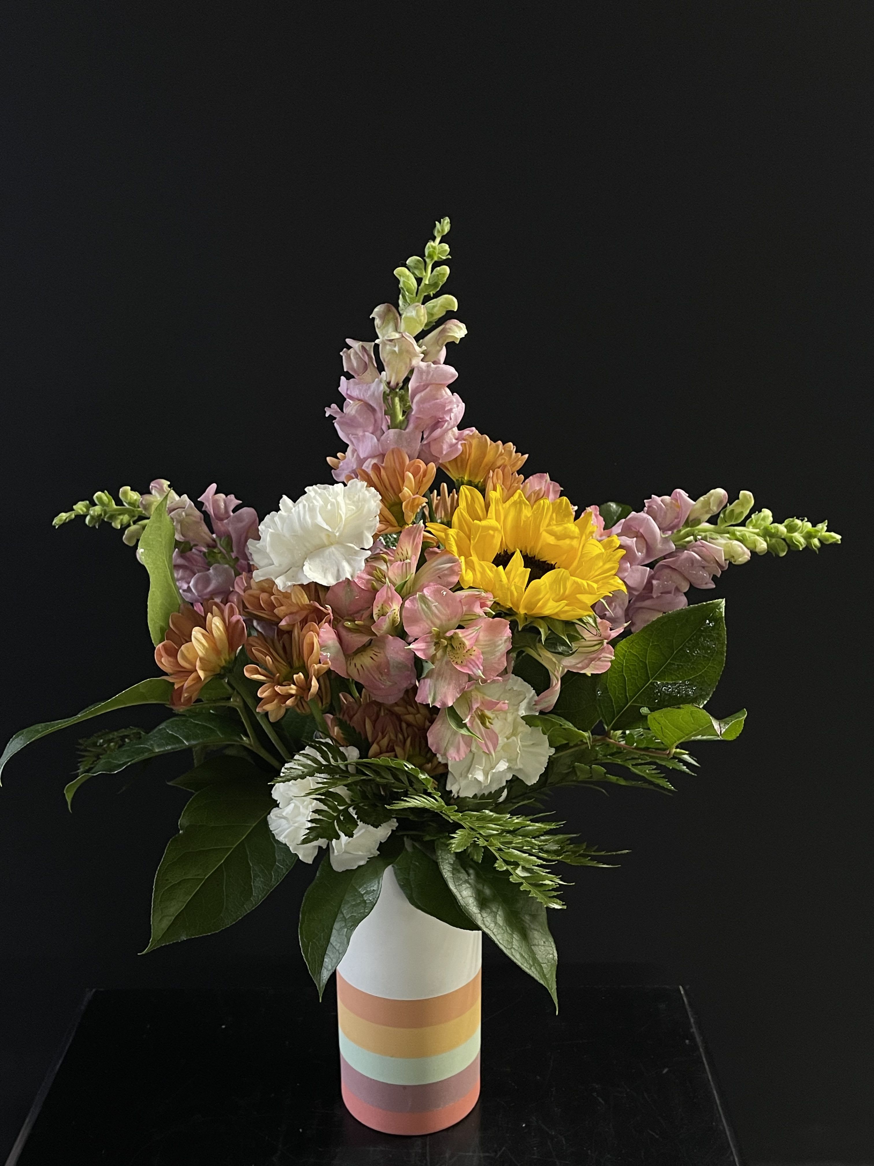 Mixed bouquet in a striped vase with sunflowers, snapdragons, and carnations