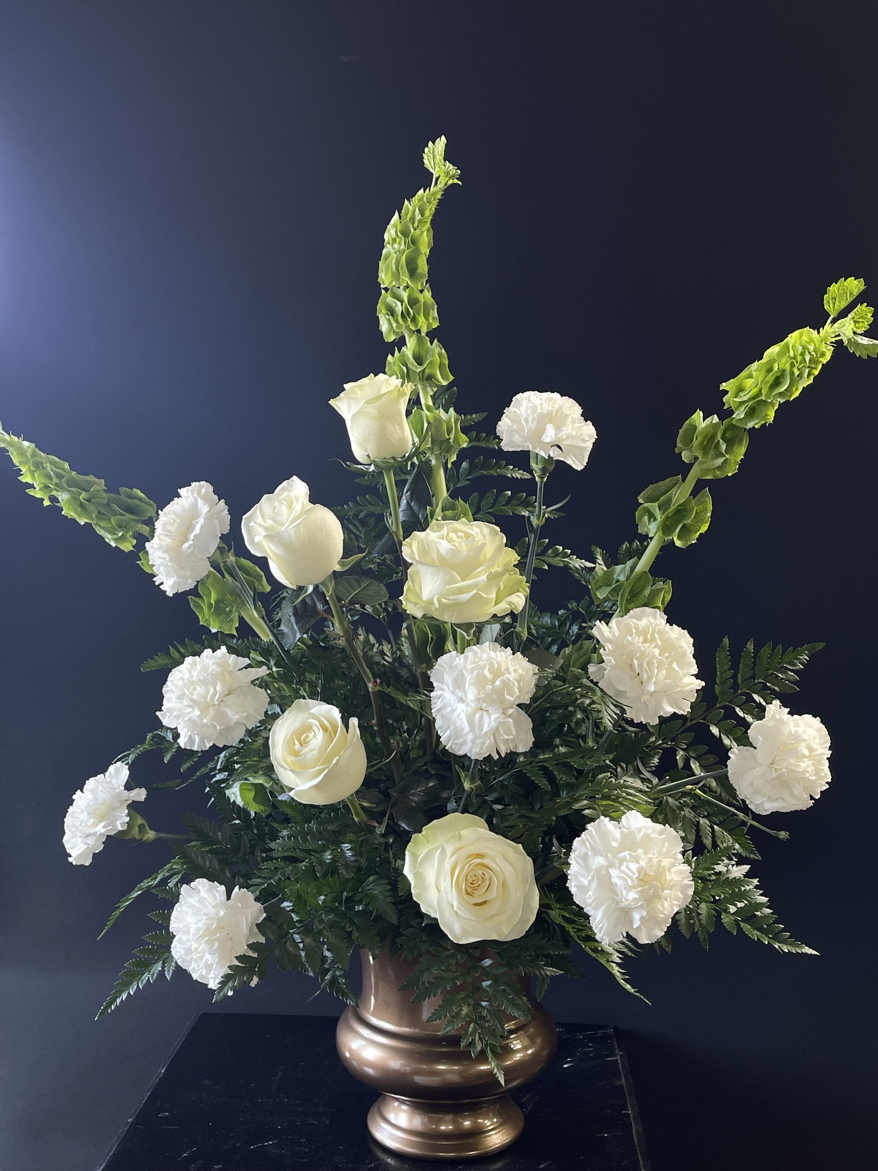 White roses and carnations in a bronze vase with tall green spikes