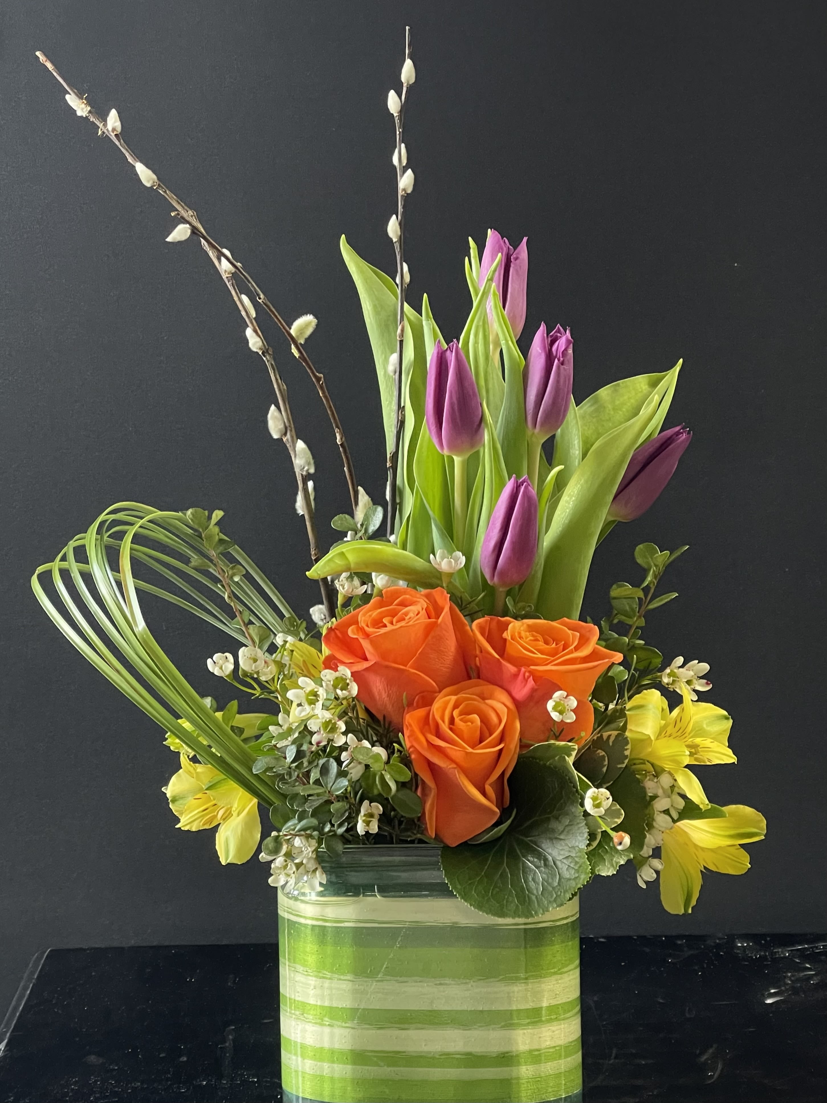 Orange roses and purple tulips in a striped glass vase