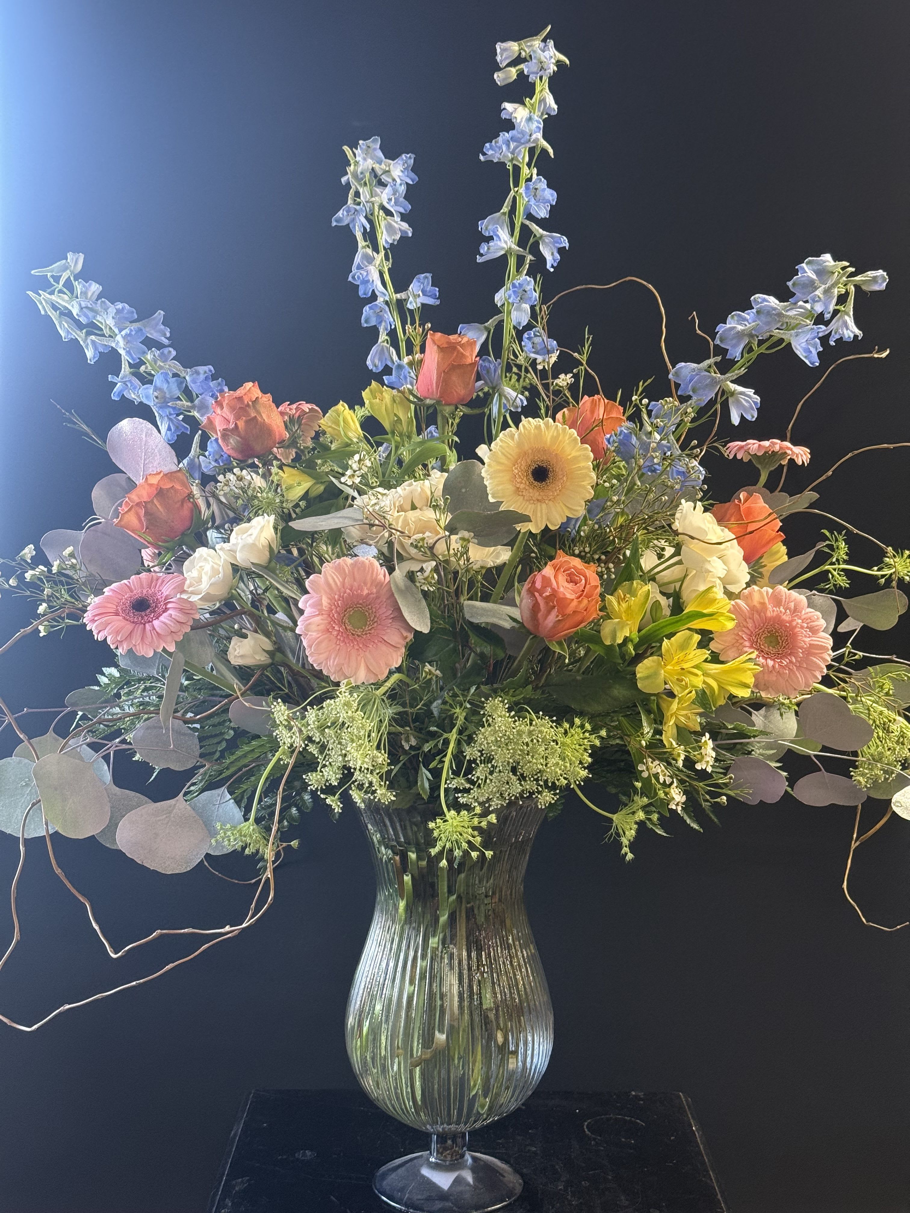 Mixed bouquet in a glass vase with blue delphinium and pink gerbera daisies