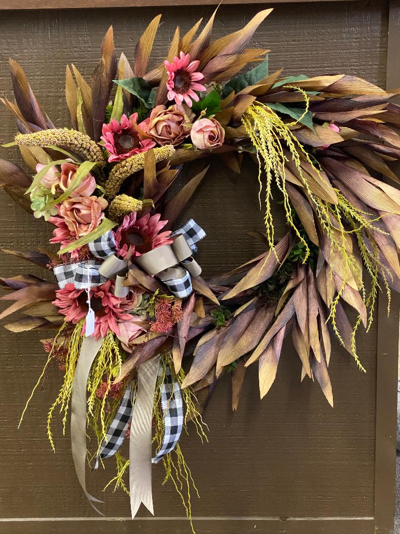 Autumn wreath with pink flowers and plaid ribbon on a brown door