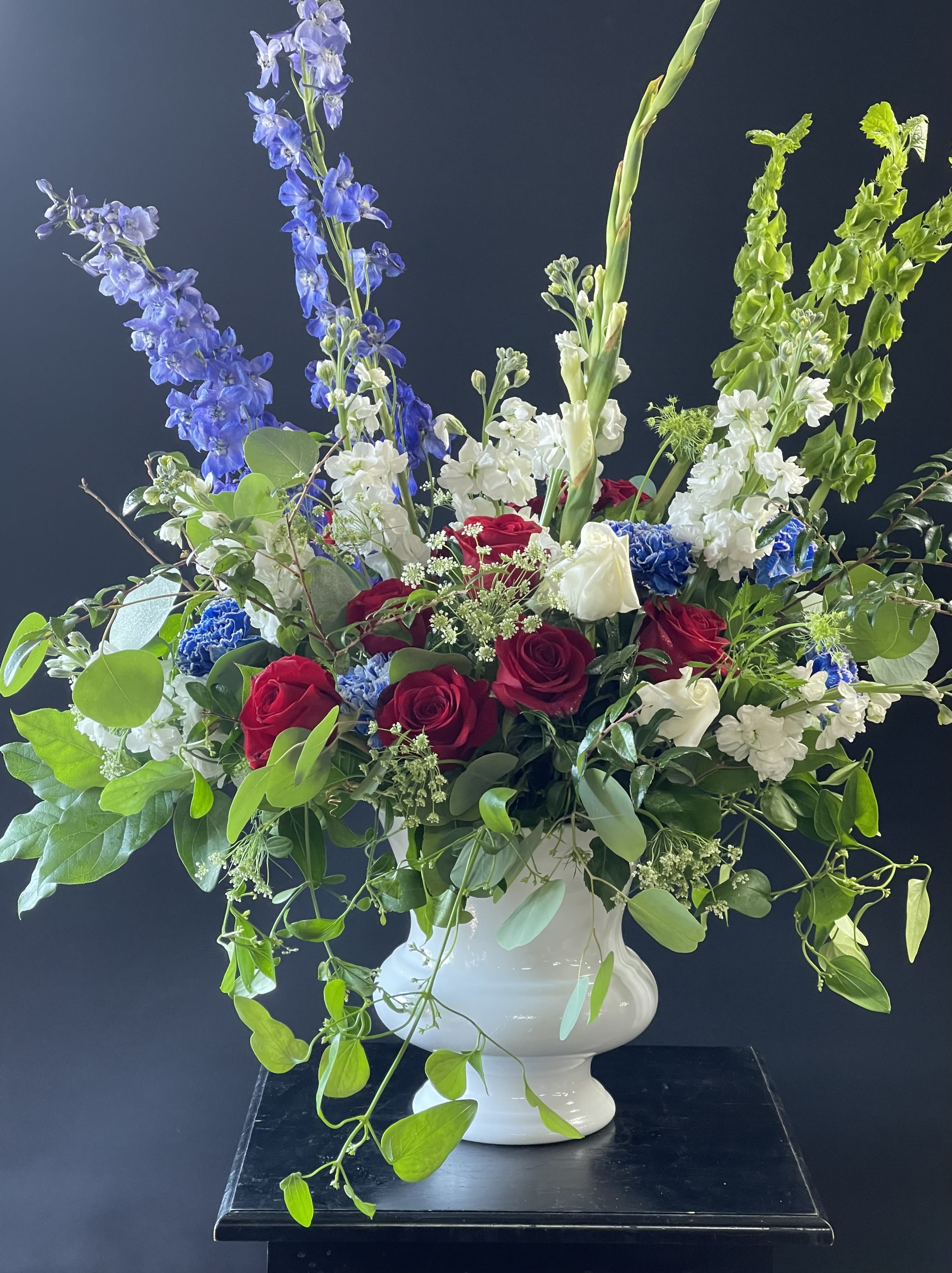 Large bouquet of red and white roses with blue delphinium in a white vase