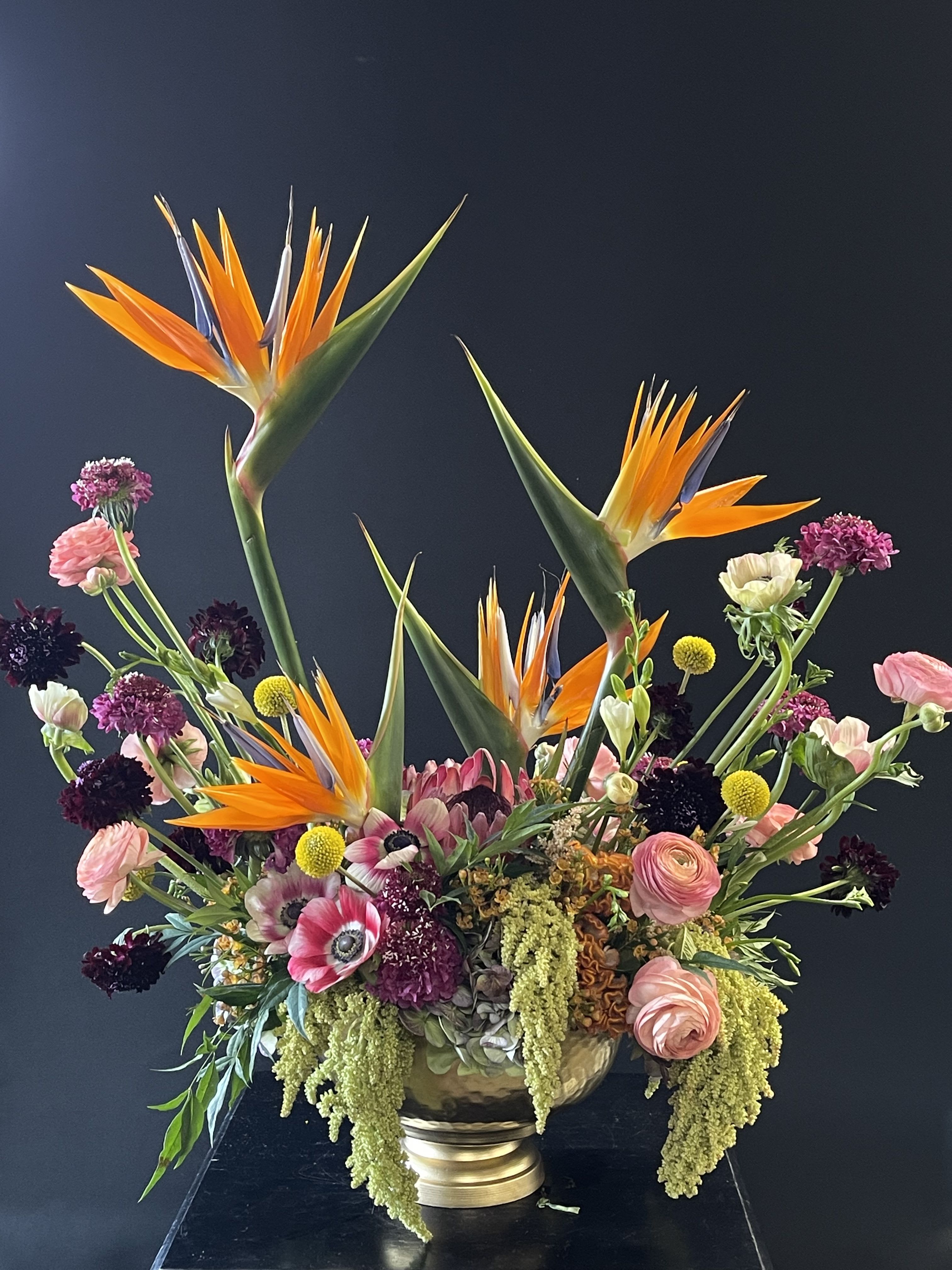Large mixed floral arrangement with orange bird-of-paradise and pink blooms in a gold vase